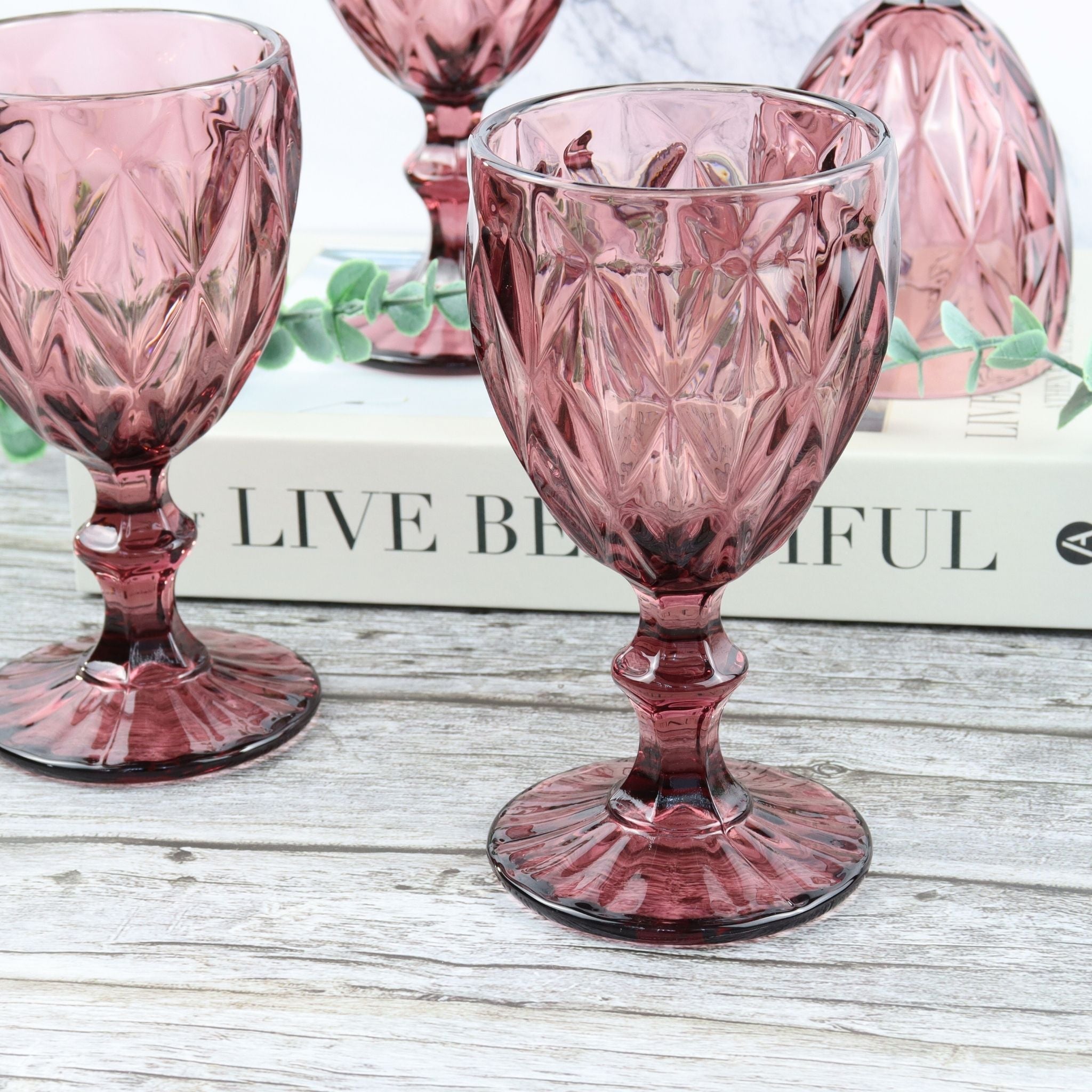 Purple glass goblets on a wooden table with an orange flower.