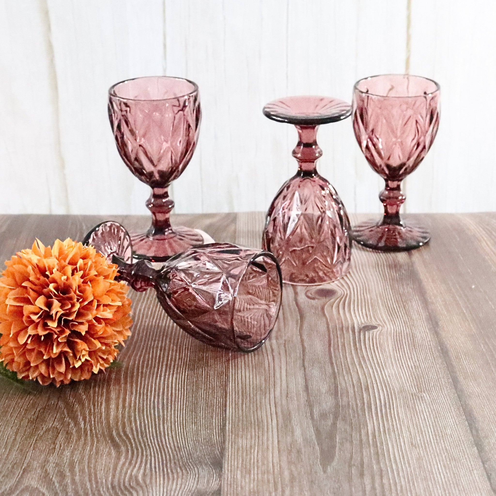 Set of purple glass goblets on a wooden surface with an orange flower.
