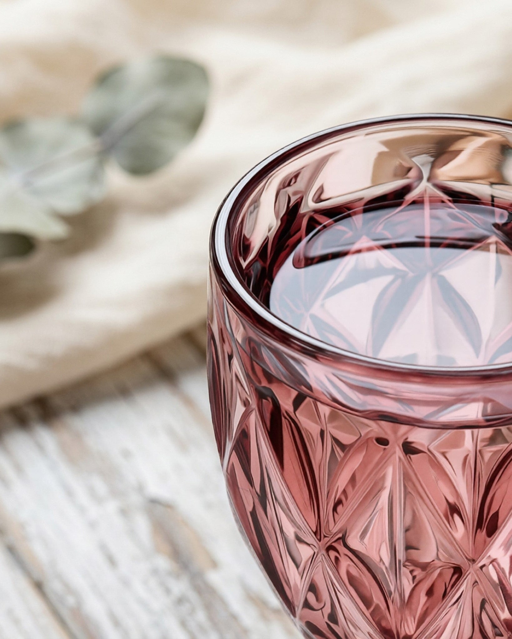 Pink crystal glass filled with a dark liquid on a wooden surface.