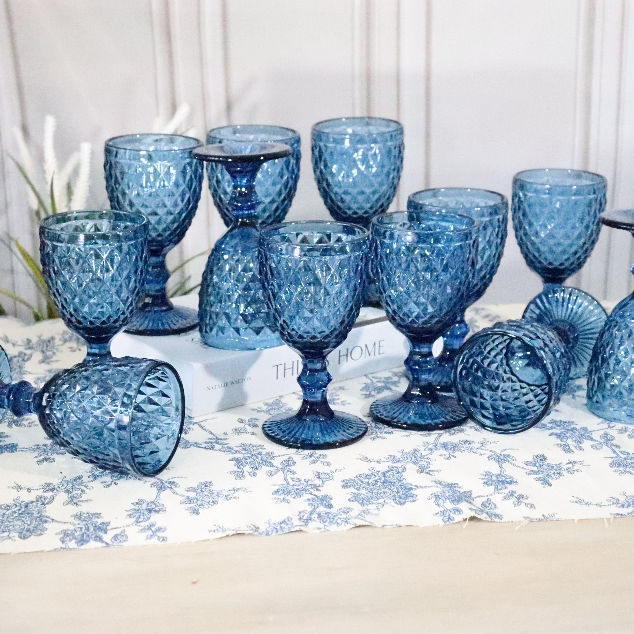 Set of blue textured glass goblets on a floral tablecloth with a white background