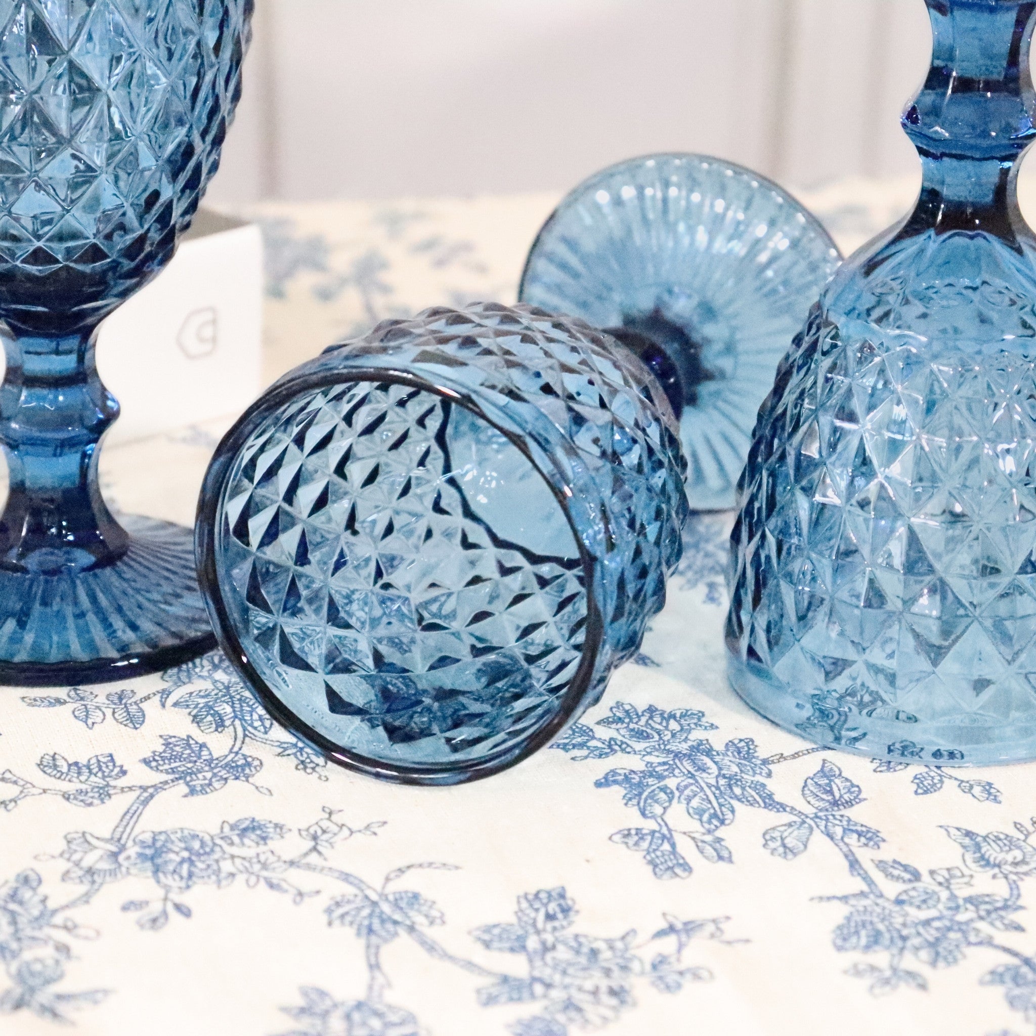 Set of blue glass tumblers with intricate patterns on a floral tablecloth.