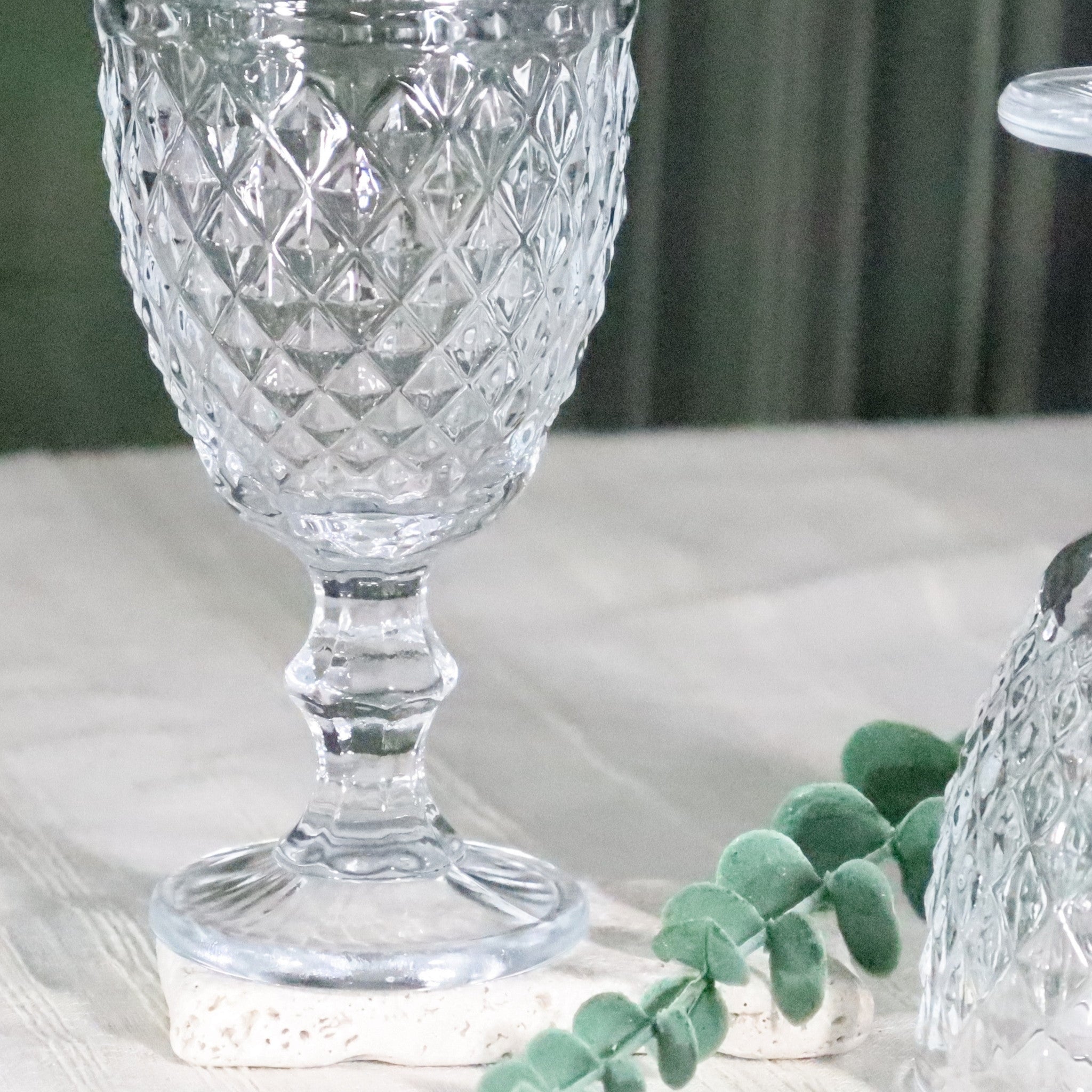 Clear glass goblet with diamond pattern on a white surface with greenery