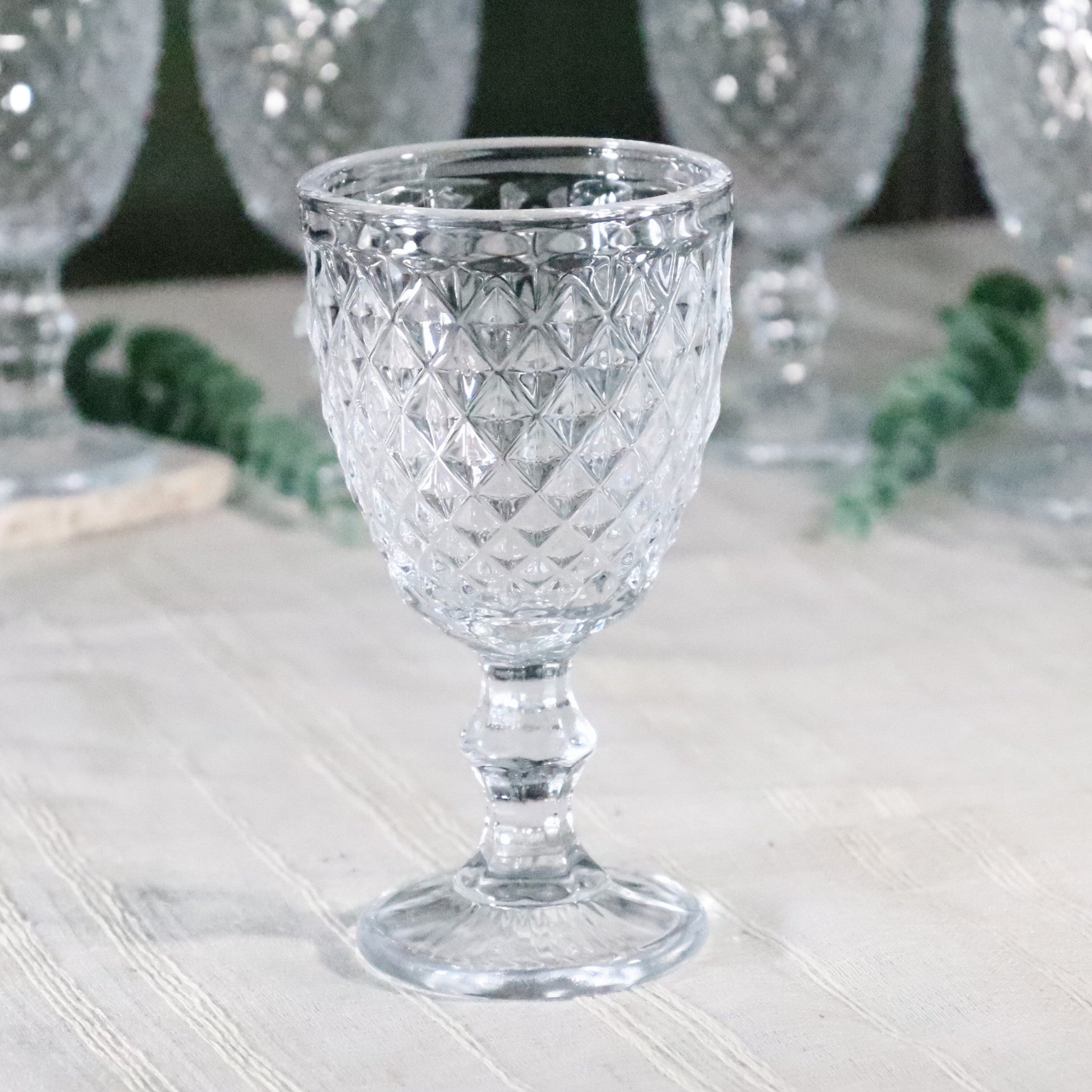 Clear glass goblet with diamond pattern on a light wooden surface