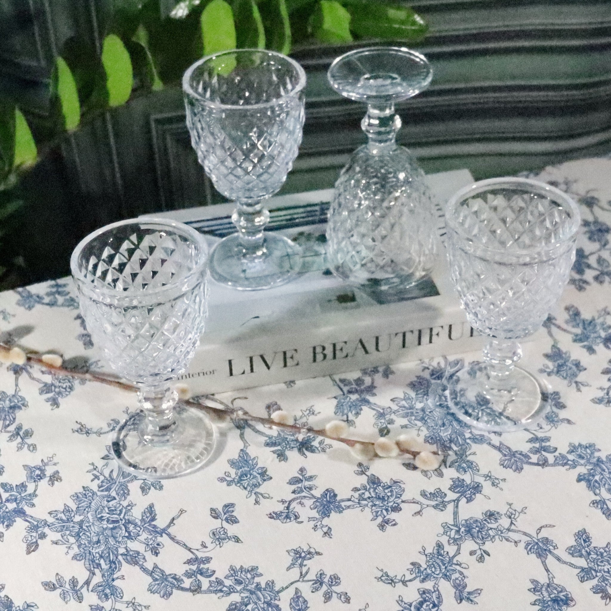 Set of clear glass goblets on a book with a floral tablecloth in the background
