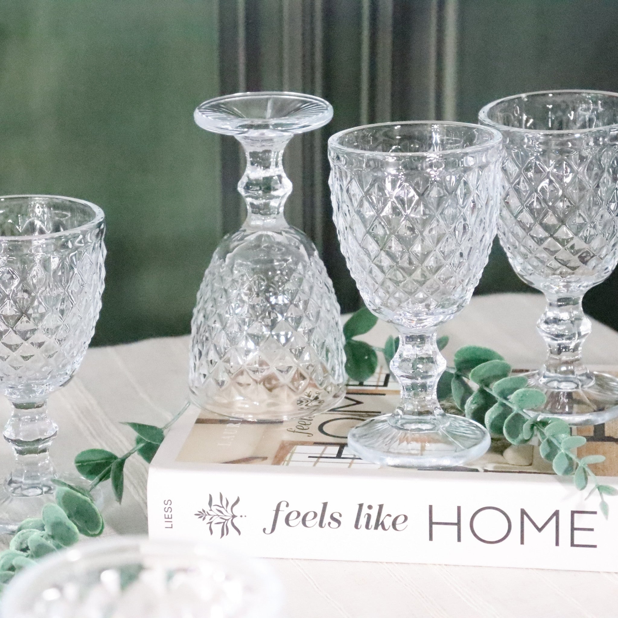Clear glass goblets on a book with 'feels like HOME' text in the background
