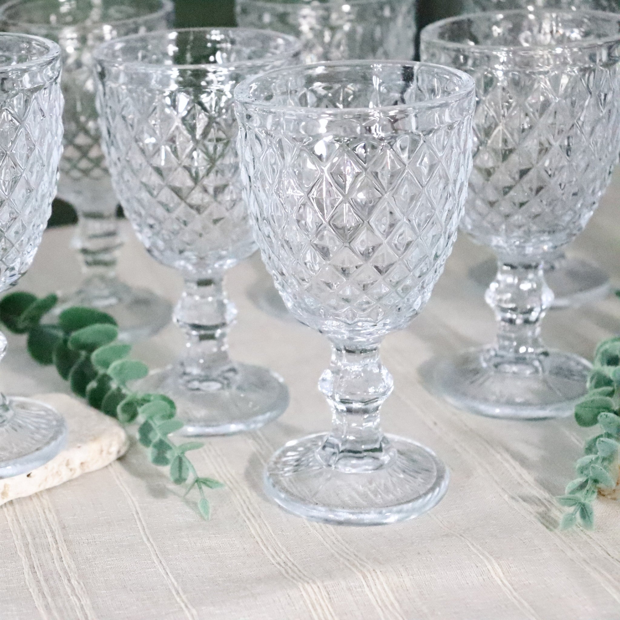 Set of clear glass goblets on a table with greenery