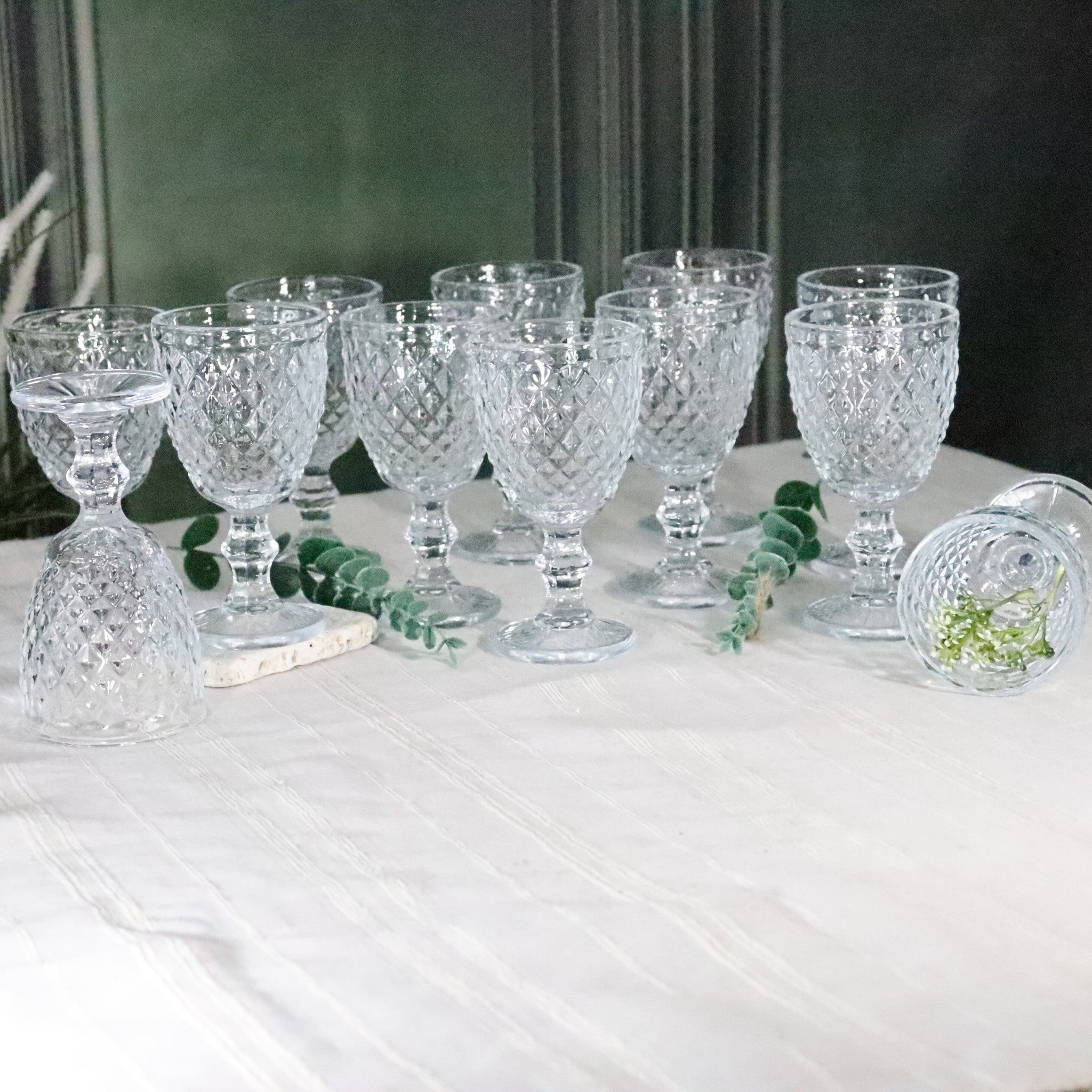 Set of crystal glasses on a white tablecloth with greenery