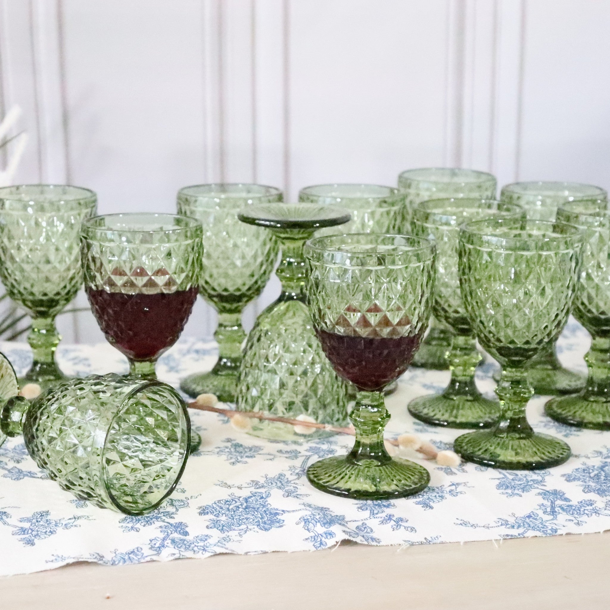 Set of green glass goblets with red liquid on a floral tablecloth.