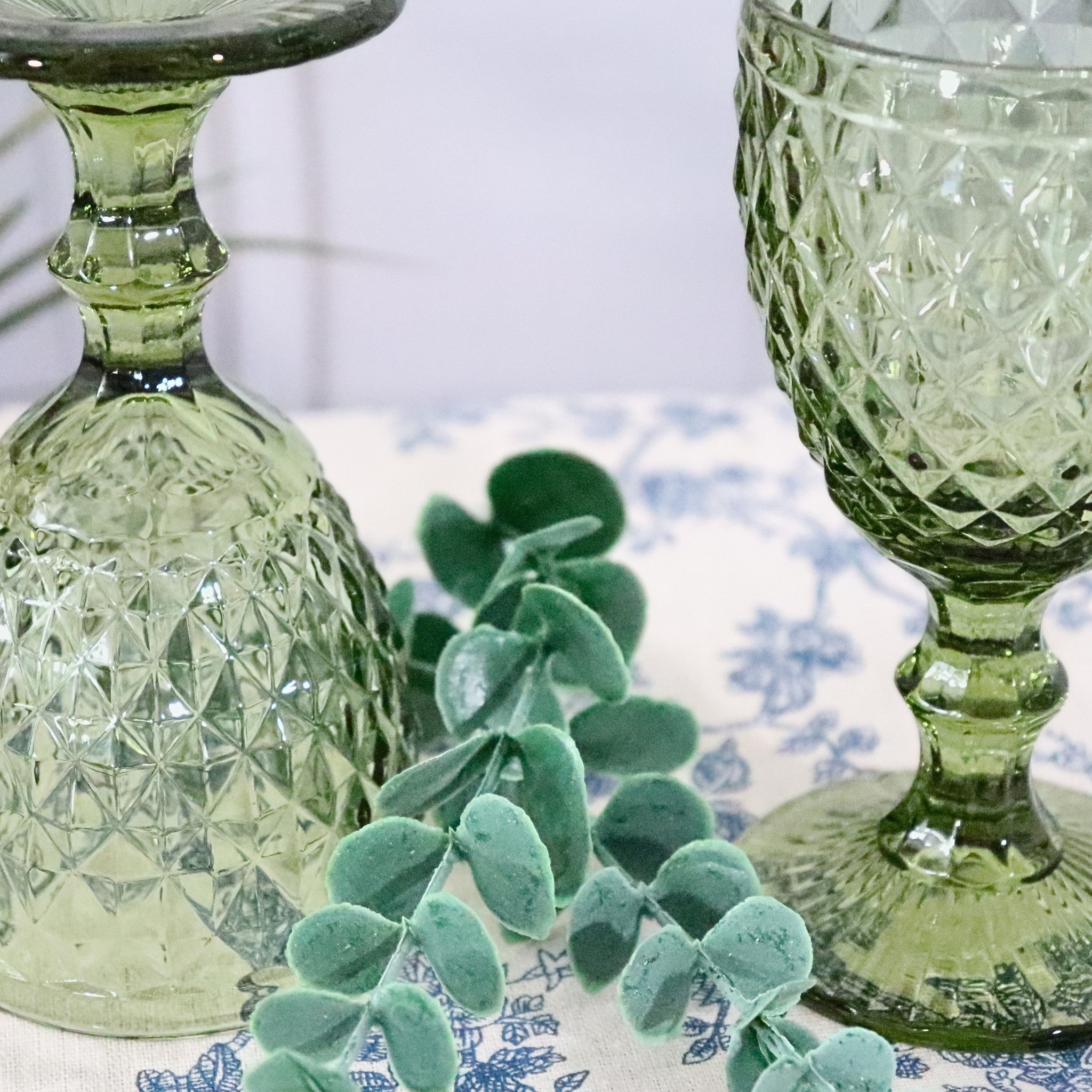 Two green glass goblets with intricate patterns on a decorative tablecloth.