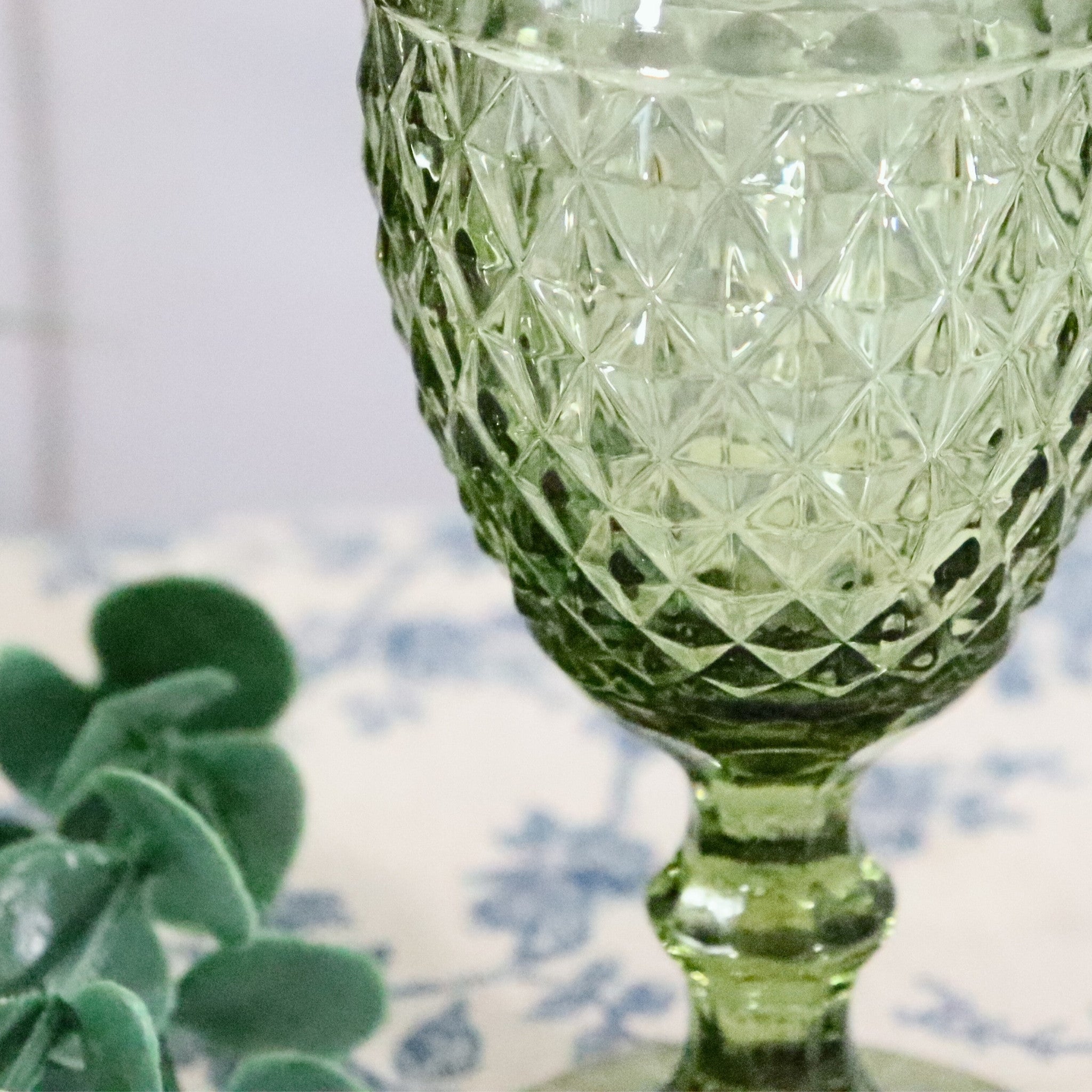 Green glass goblet with diamond pattern on a floral tablecloth