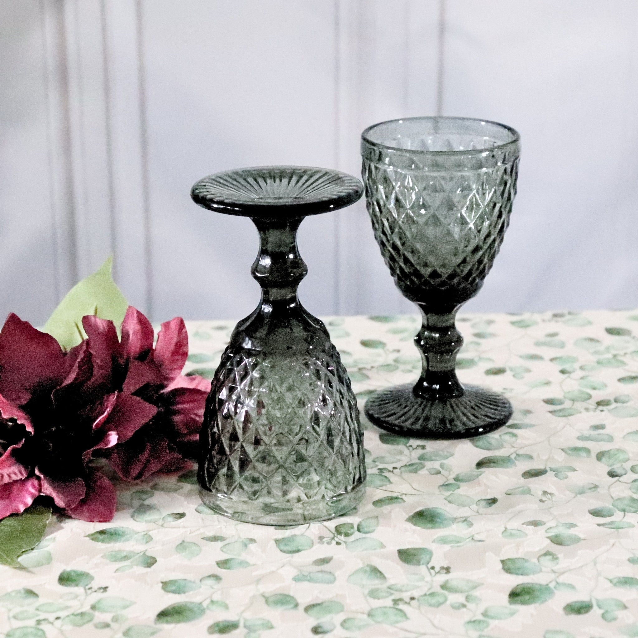 Two textured glass goblets on a patterned surface with a pink flower.