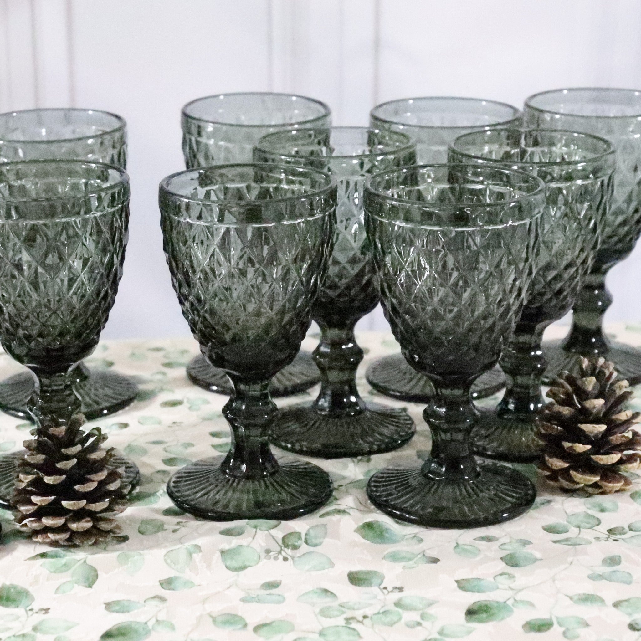 Set of textured glass goblets on a decorative surface with pinecones.