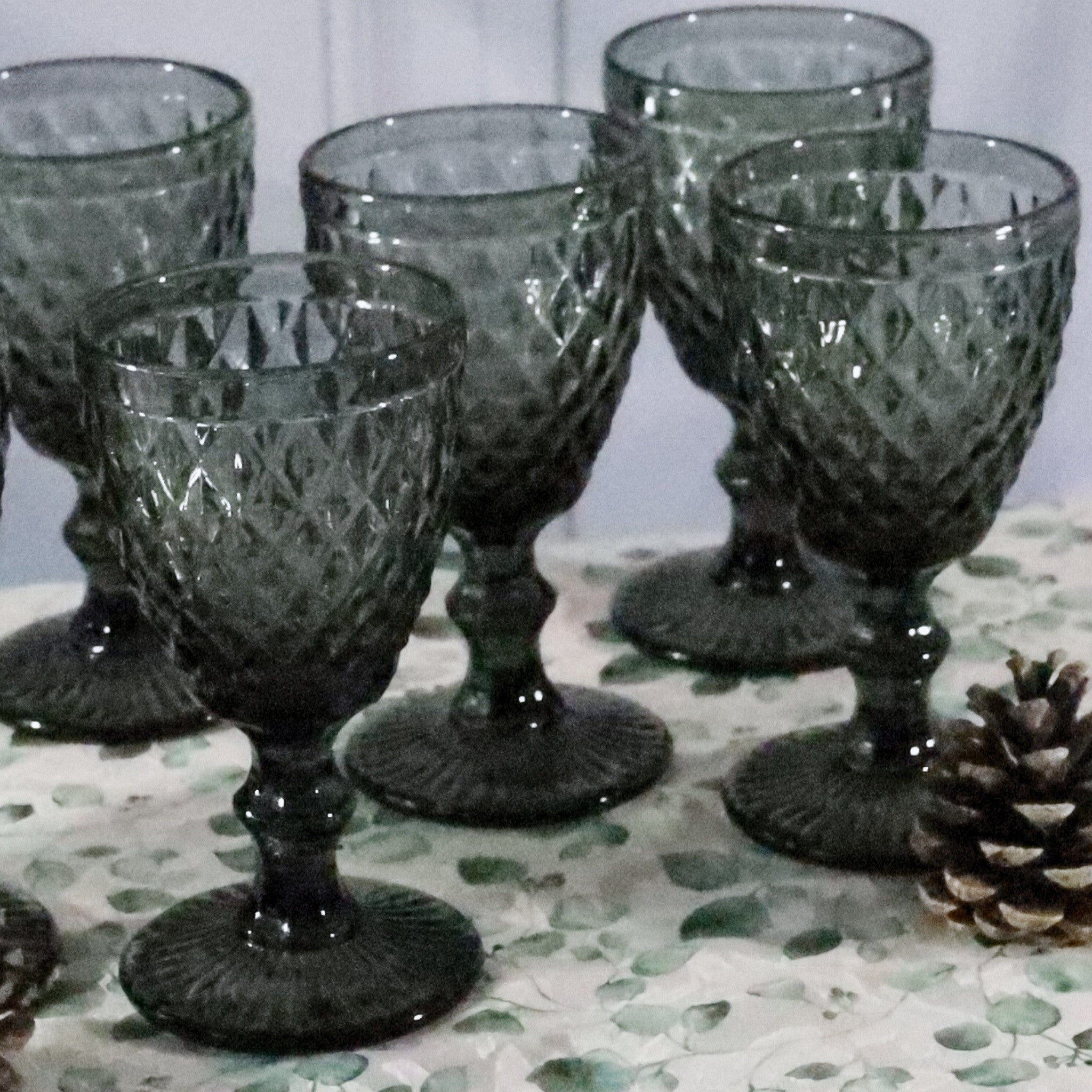 Set of six green glass goblets on a patterned surface with a pine cone.