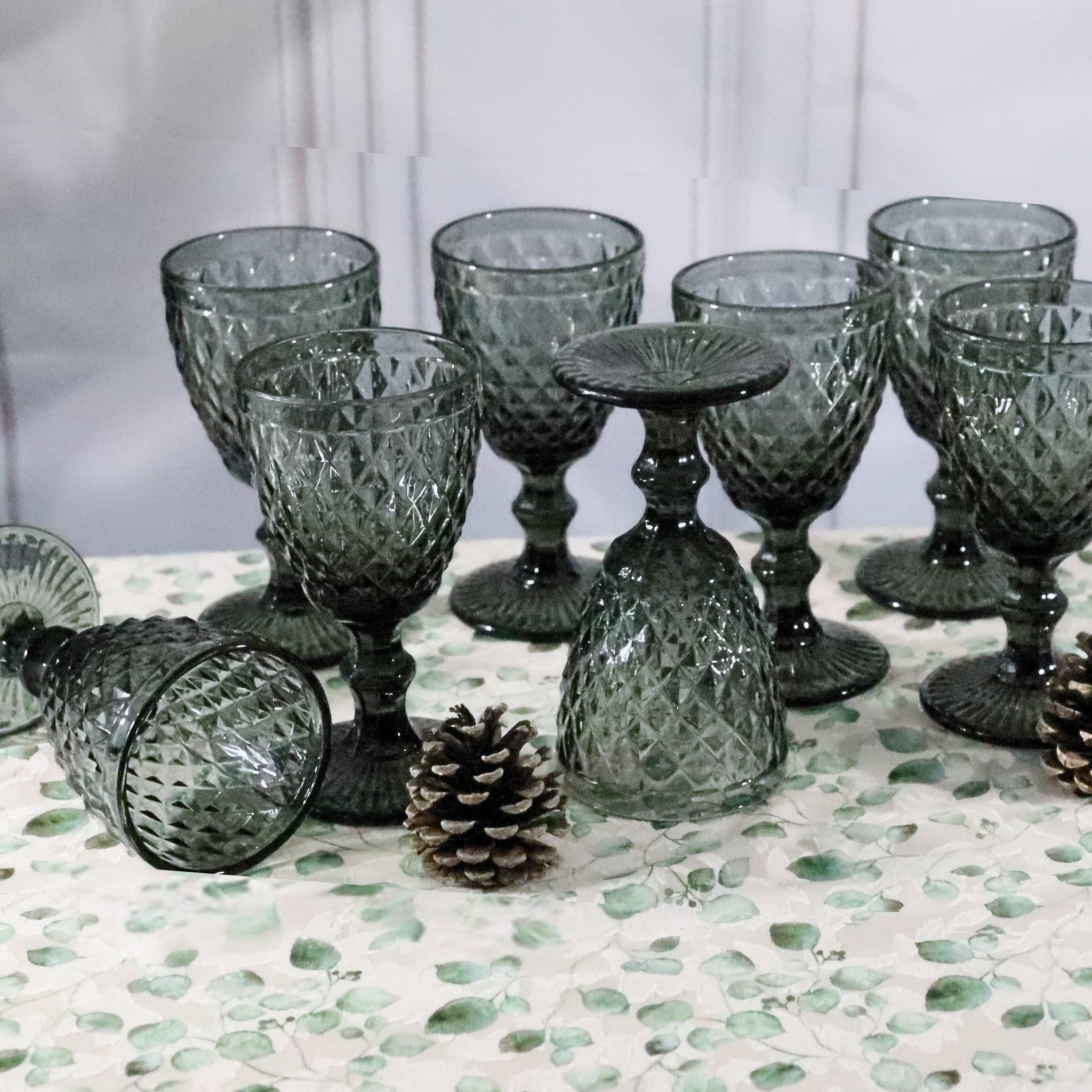 Set of textured green glass goblets on a decorative surface with pinecones.
