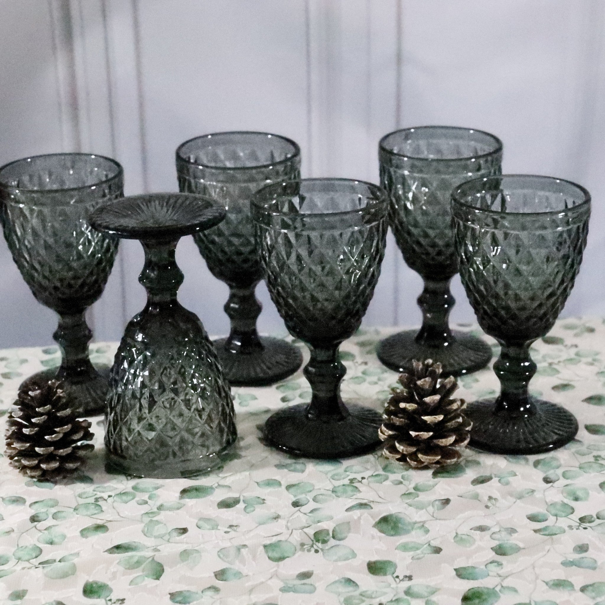 Set of dark glass goblets on a decorative surface with pinecones.