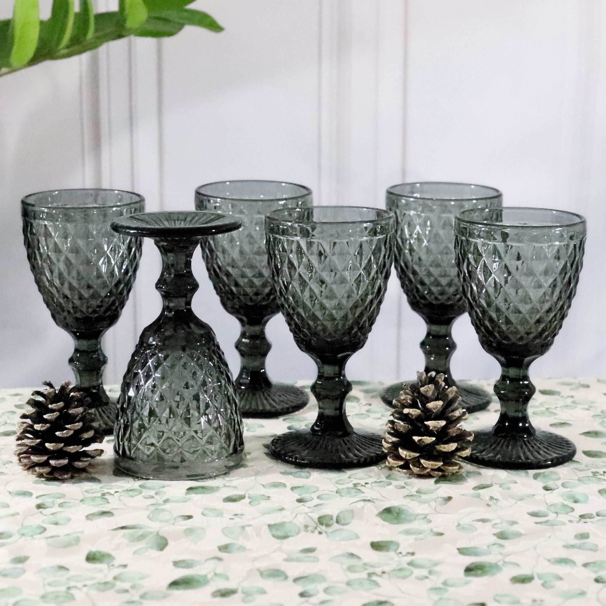 Set of textured gray glass goblets on a decorative surface with pinecones.