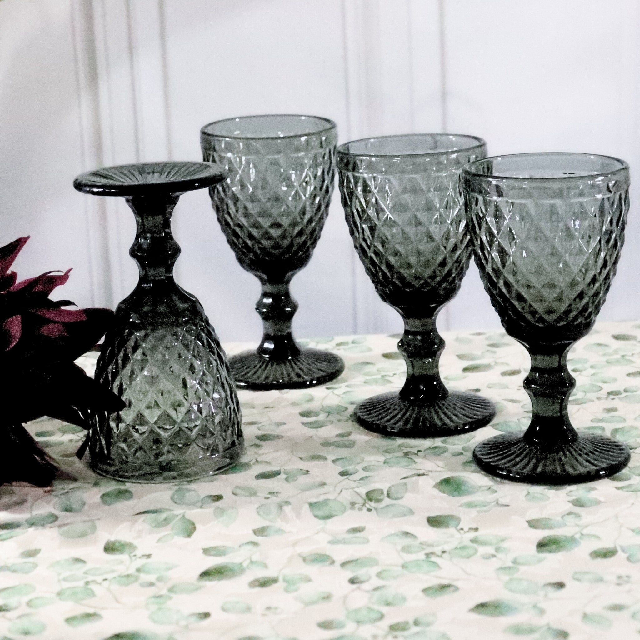 Set of four dark grey embossed glass goblets on a white surface with a white background