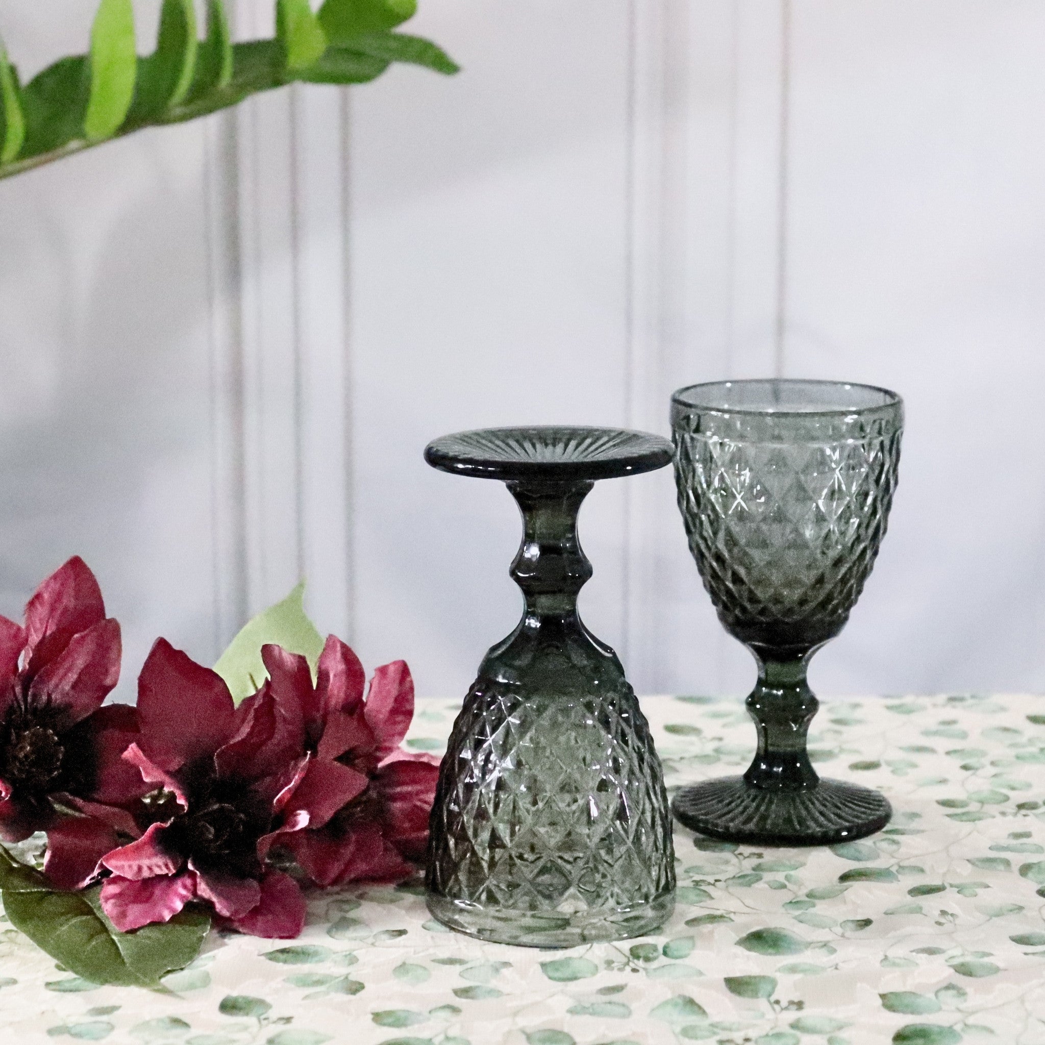 Two green glass goblets on a table with flowers and leaves.