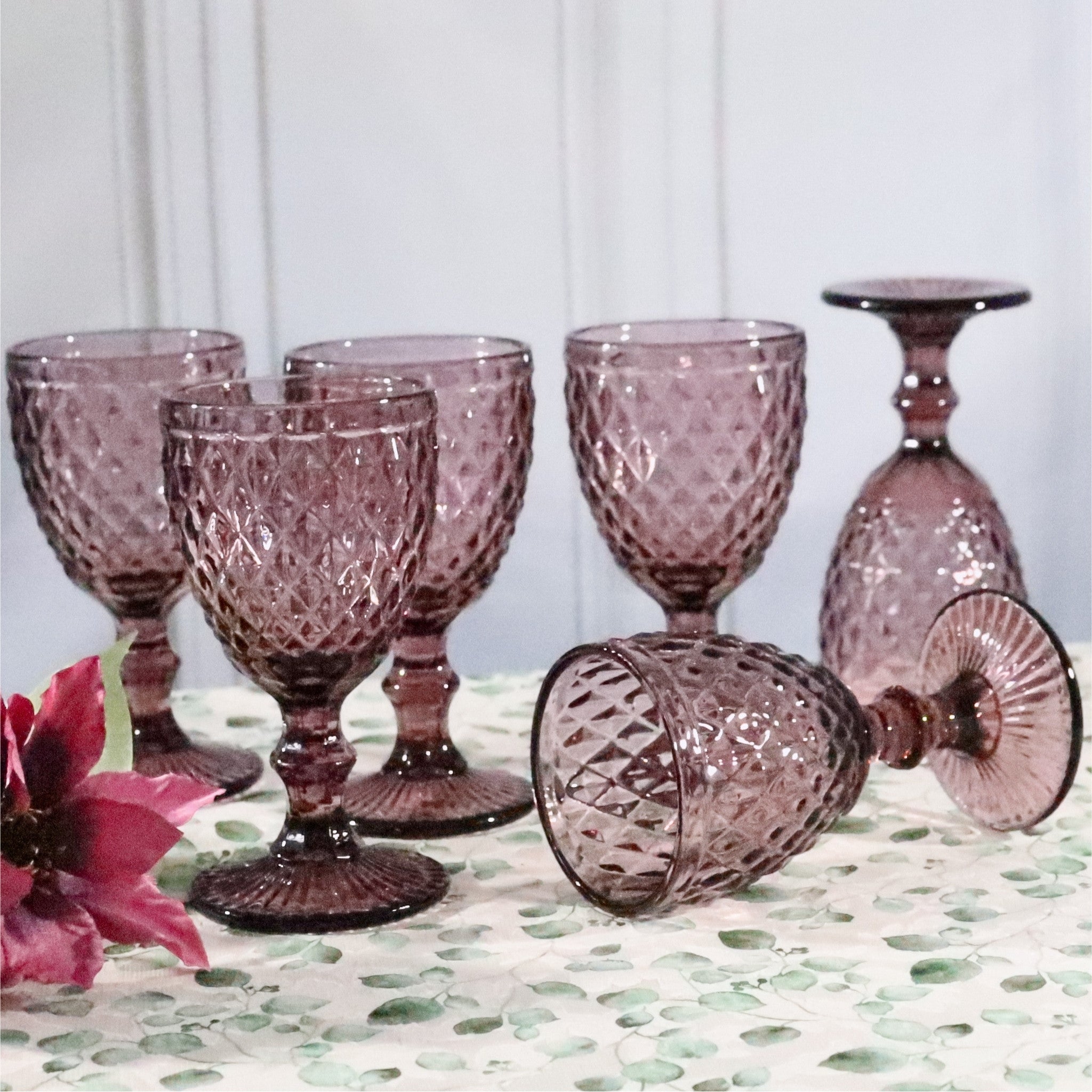 Set of purple glass goblets on a patterned surface with a white background