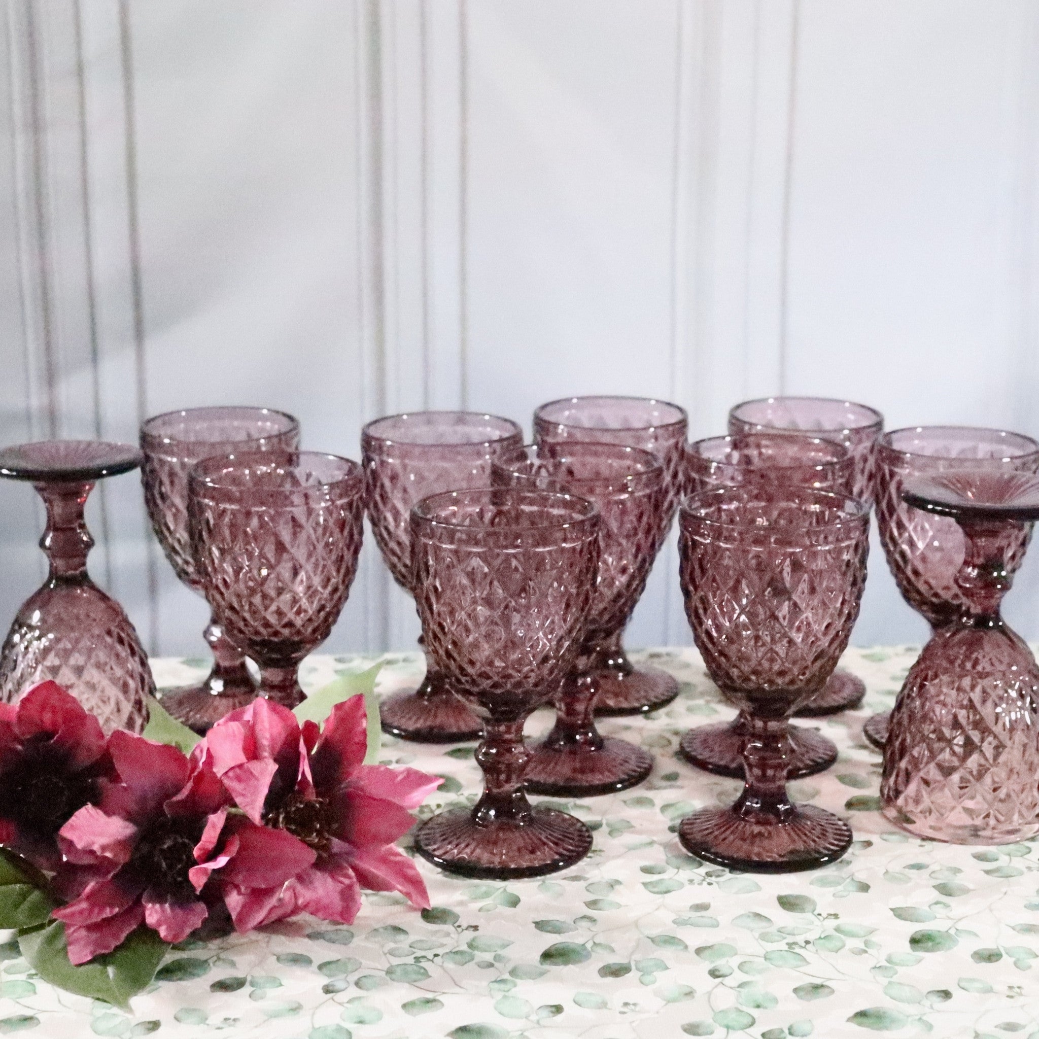 Set of purple glass goblets on a table with flowers and a white background