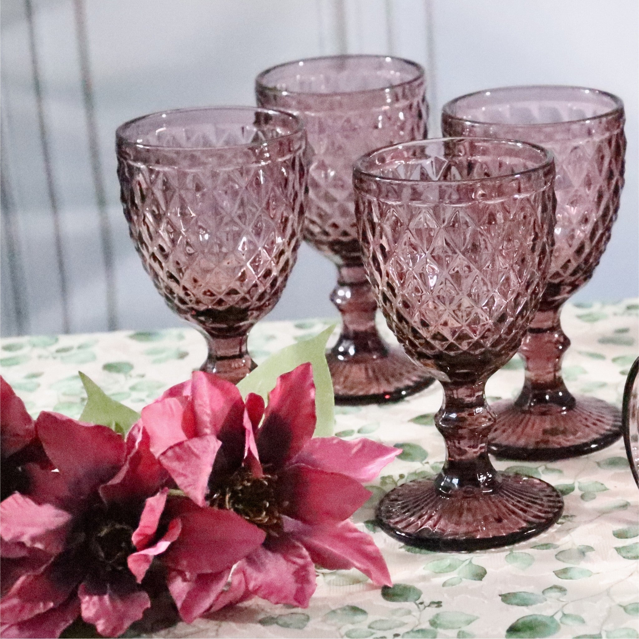 Set of four purple patterned glasses on a table with pink flowers.