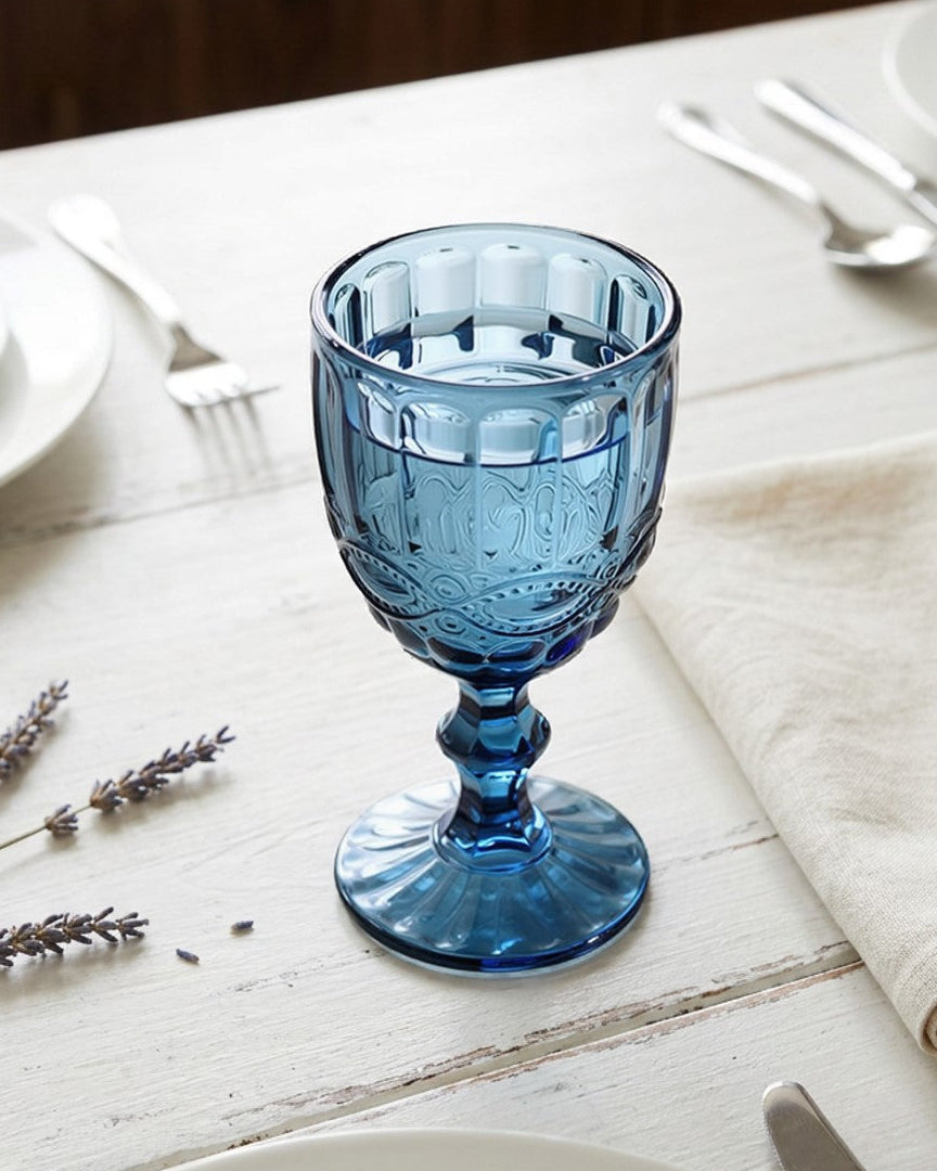 Blue glass goblet on a white wooden table with plates, silverware, and lavender.