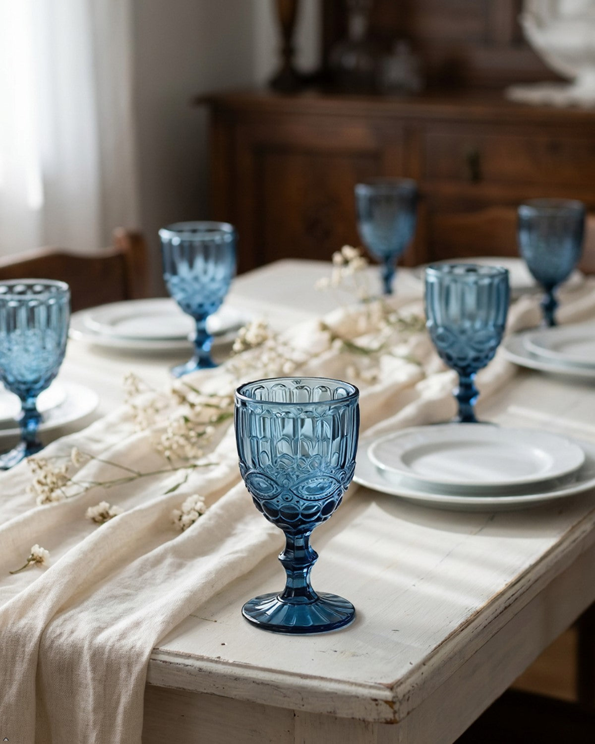 Blue glass goblets on a white tablecloth with a wooden cabinet in the background