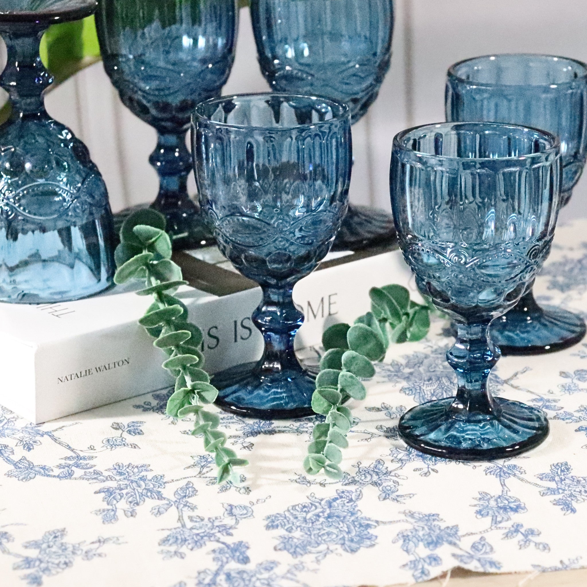 Set of blue glass goblets on a table with a floral tablecloth