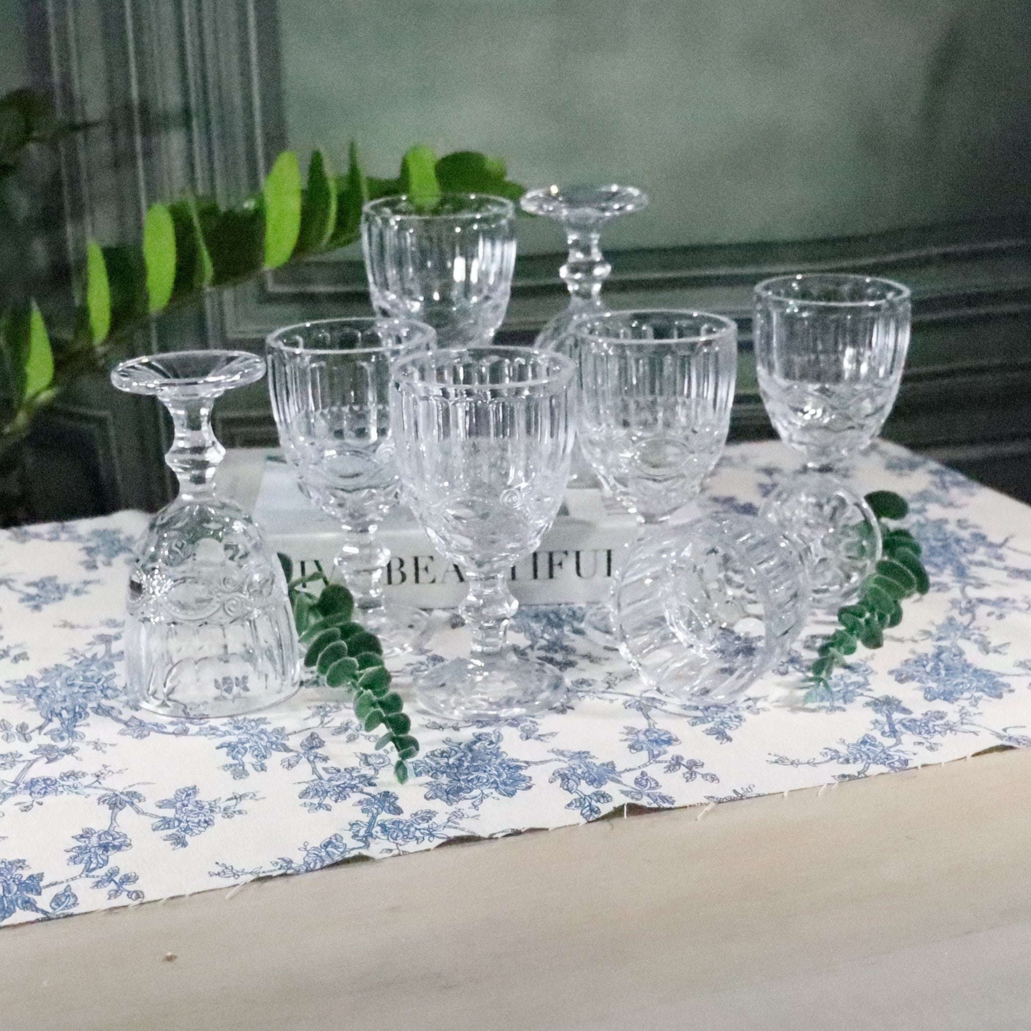 Set of clear glass tumblers on a floral tablecloth with decorative elements.
