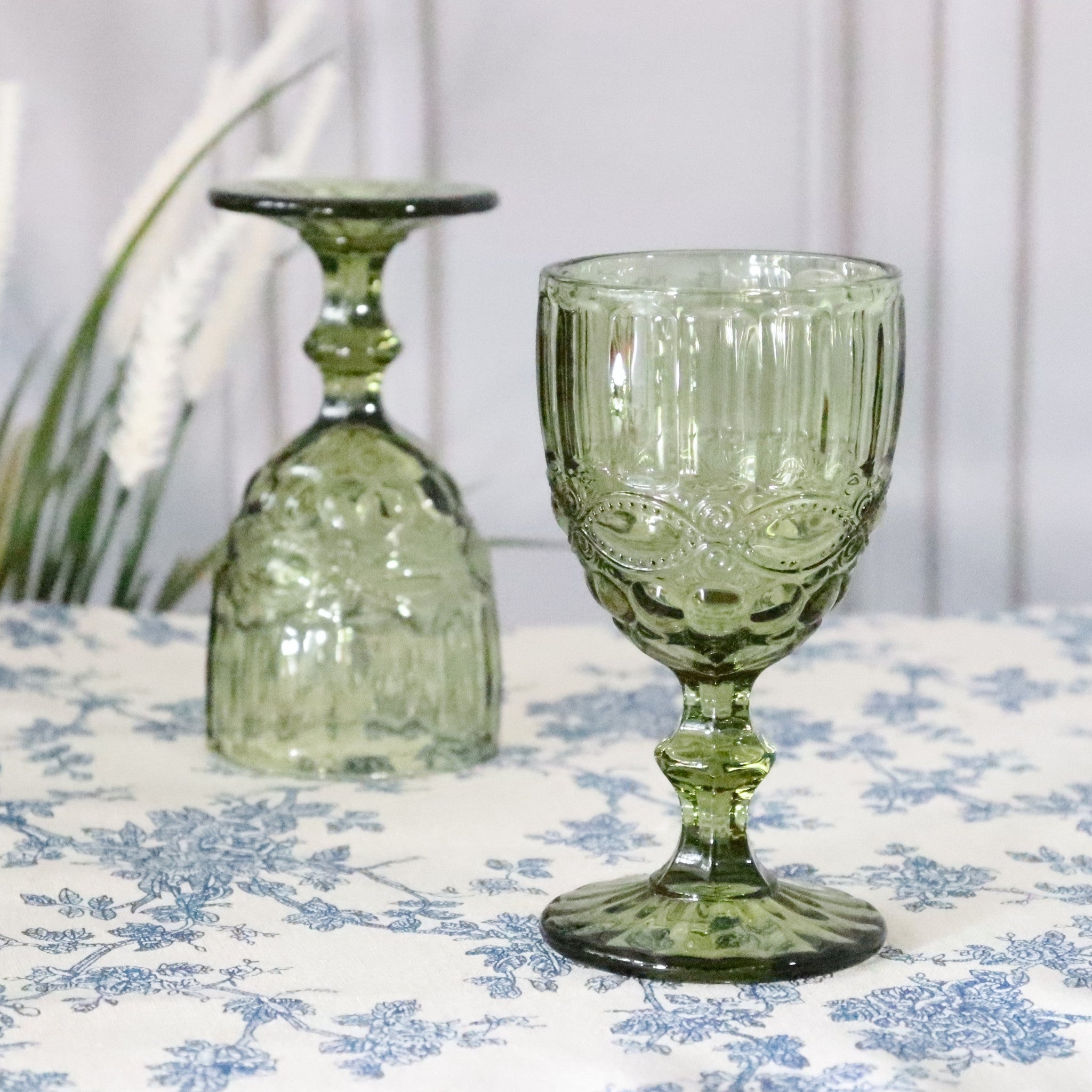 Two green glass goblets on a floral tablecloth with a white background