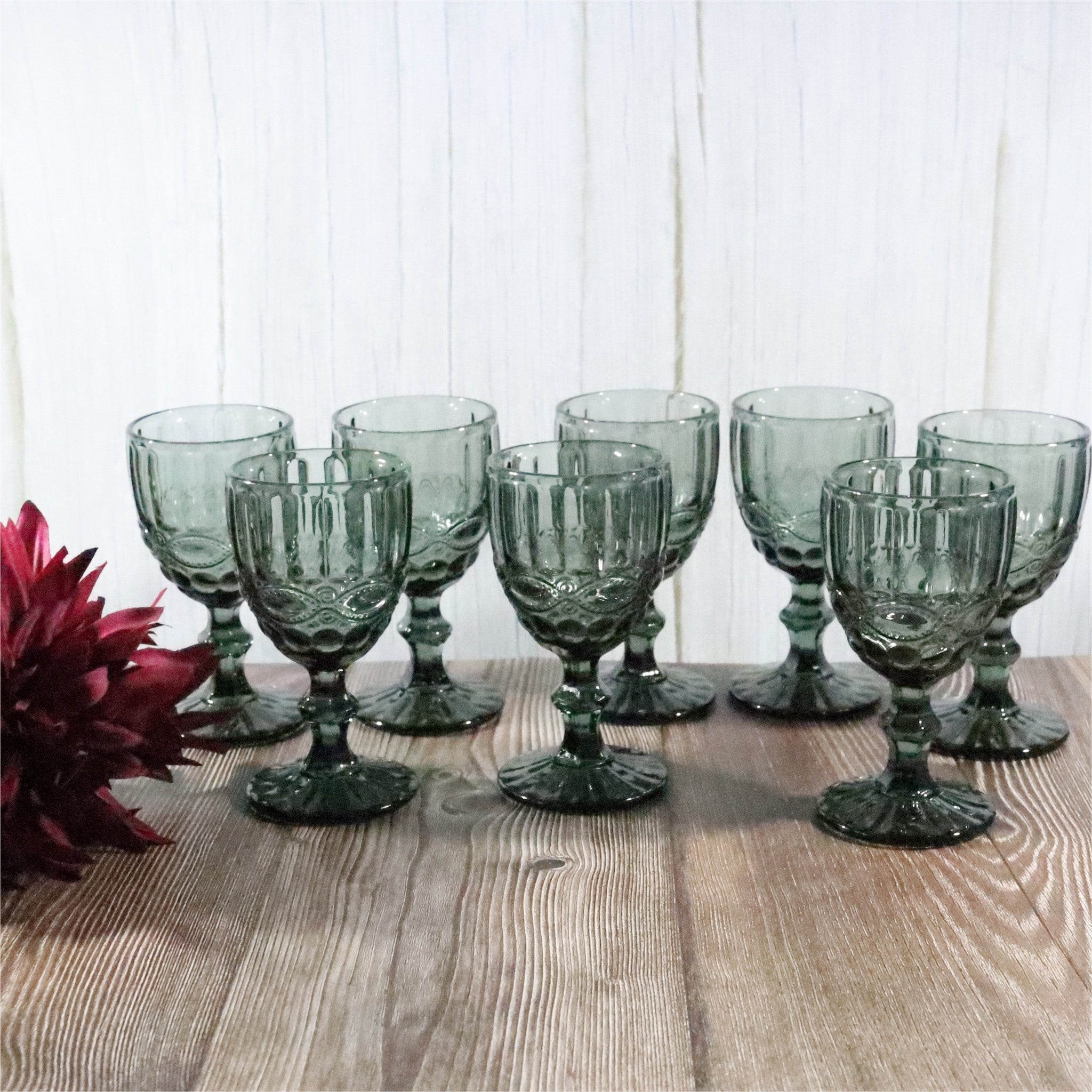 Set of grey glass goblets on a wooden table with a white paneled background