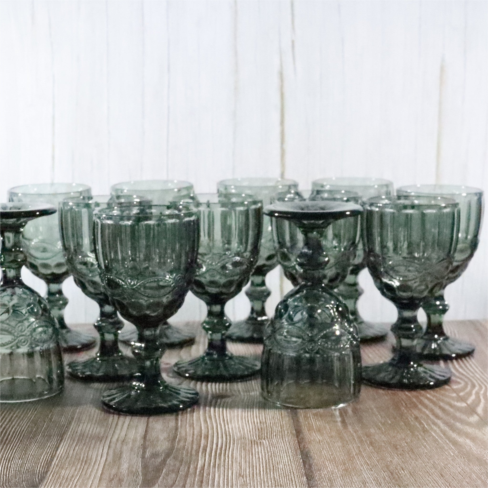 Set of grey glass goblets on a wooden surface with a white background