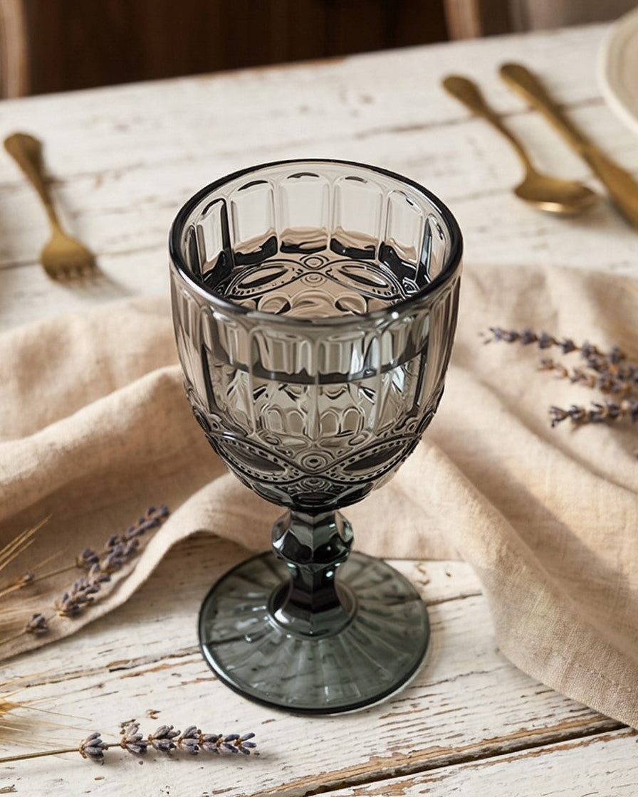 Decorative glass goblet on a table with gold cutlery and lavender, set against a wooden background.