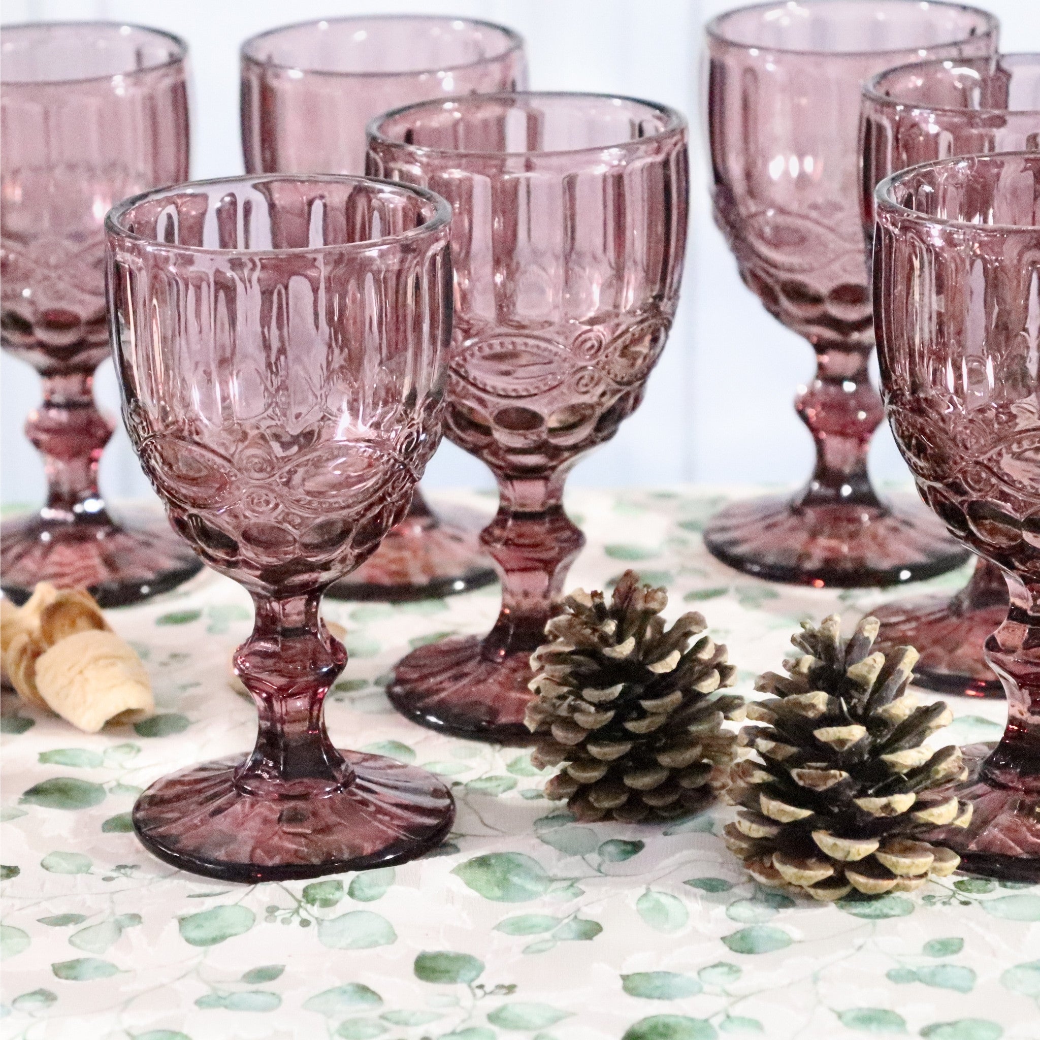 Set of pink glass goblets on a decorative tablecloth with pinecones.