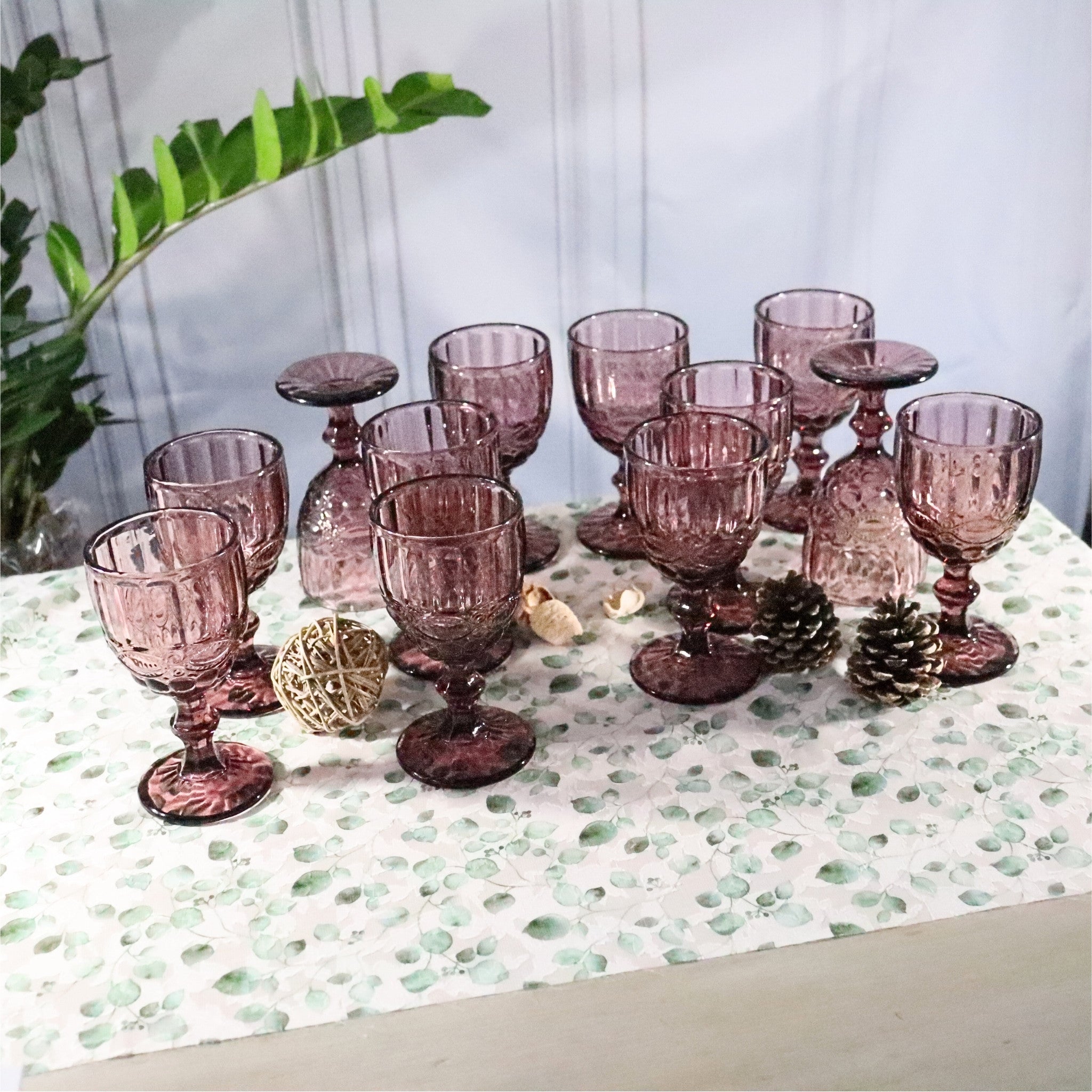 Set of purple glass goblets on a decorative tablecloth with a plant in the background