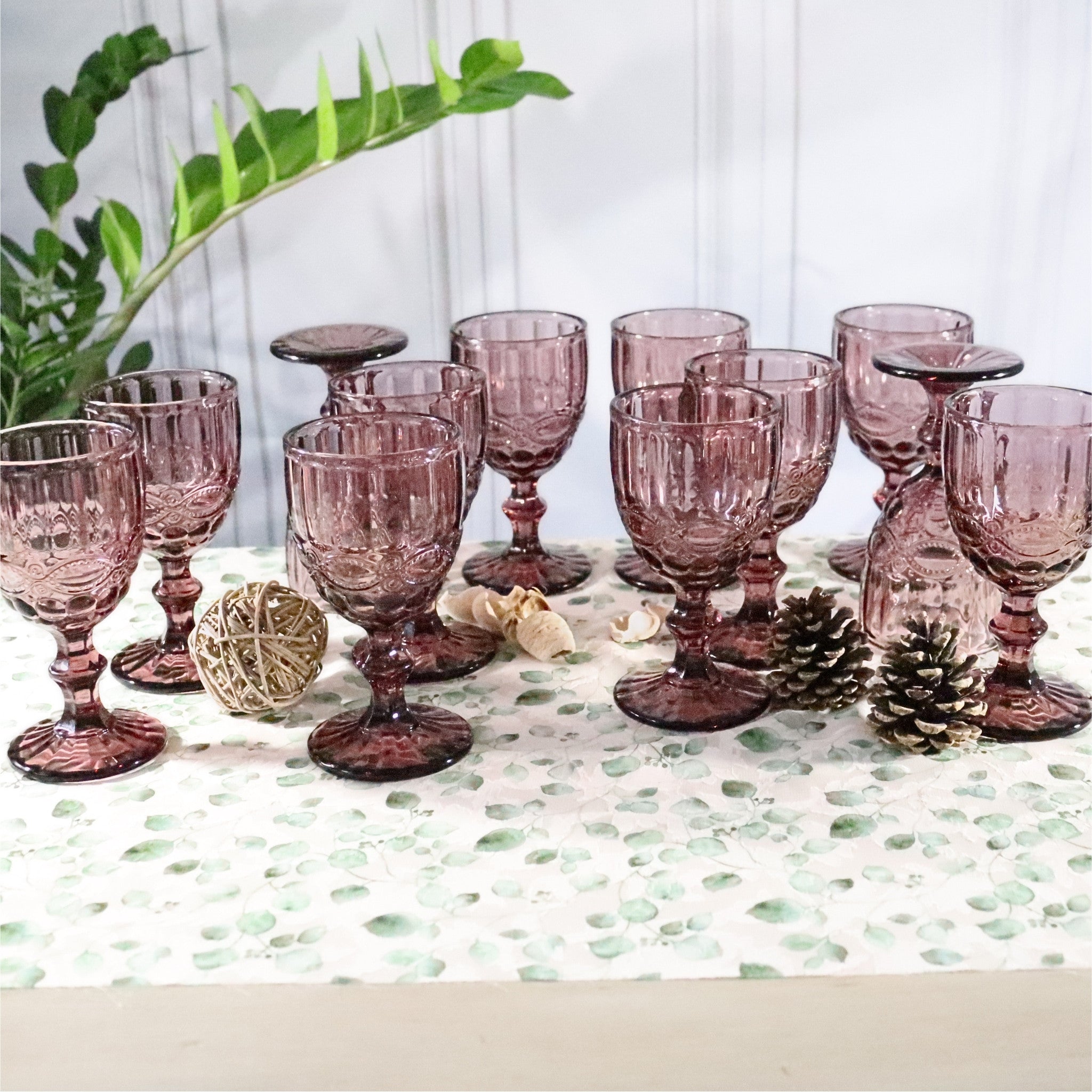Set of purple glass goblets on a decorative tablecloth with a plant in the background