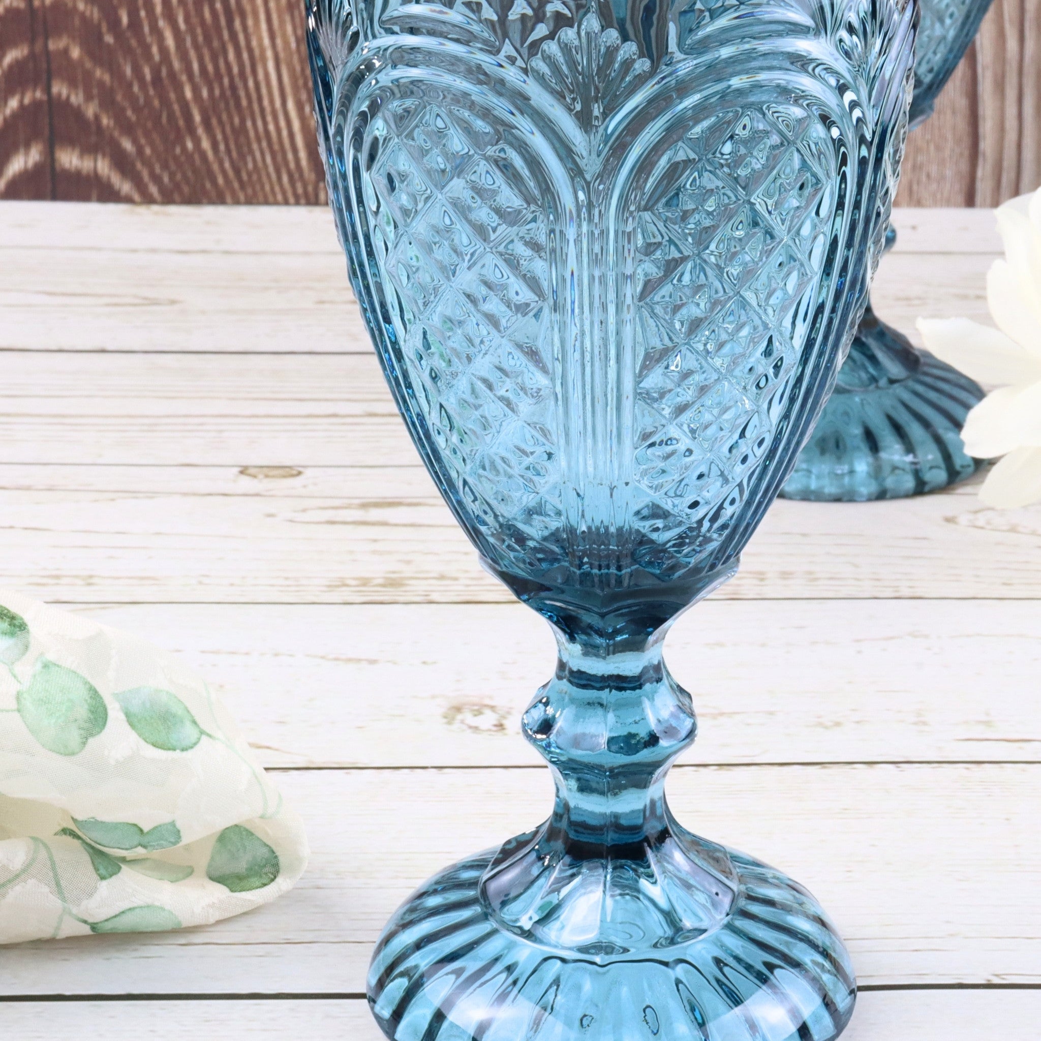 Set of blue glass goblets on a white surface with a white curtain background
