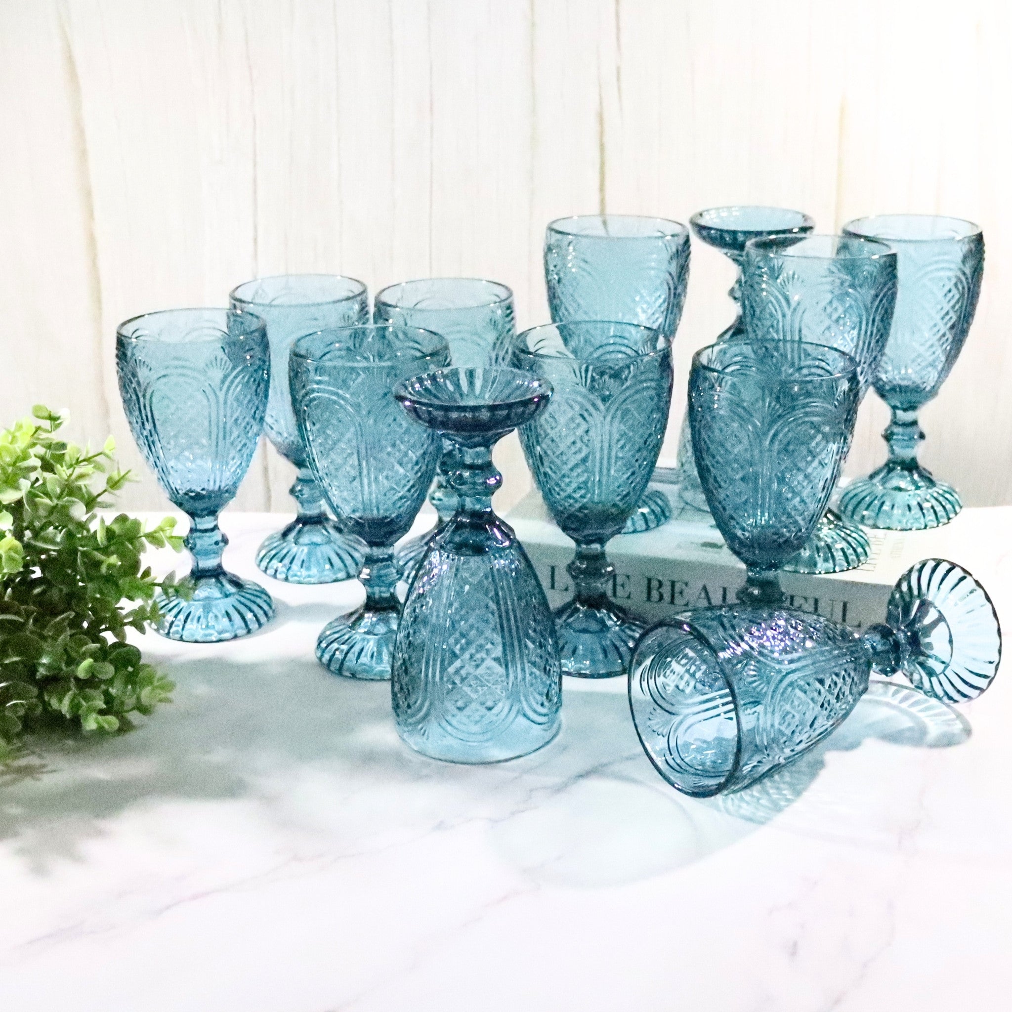 Set of blue glass goblets on a white surface with a white wooden background