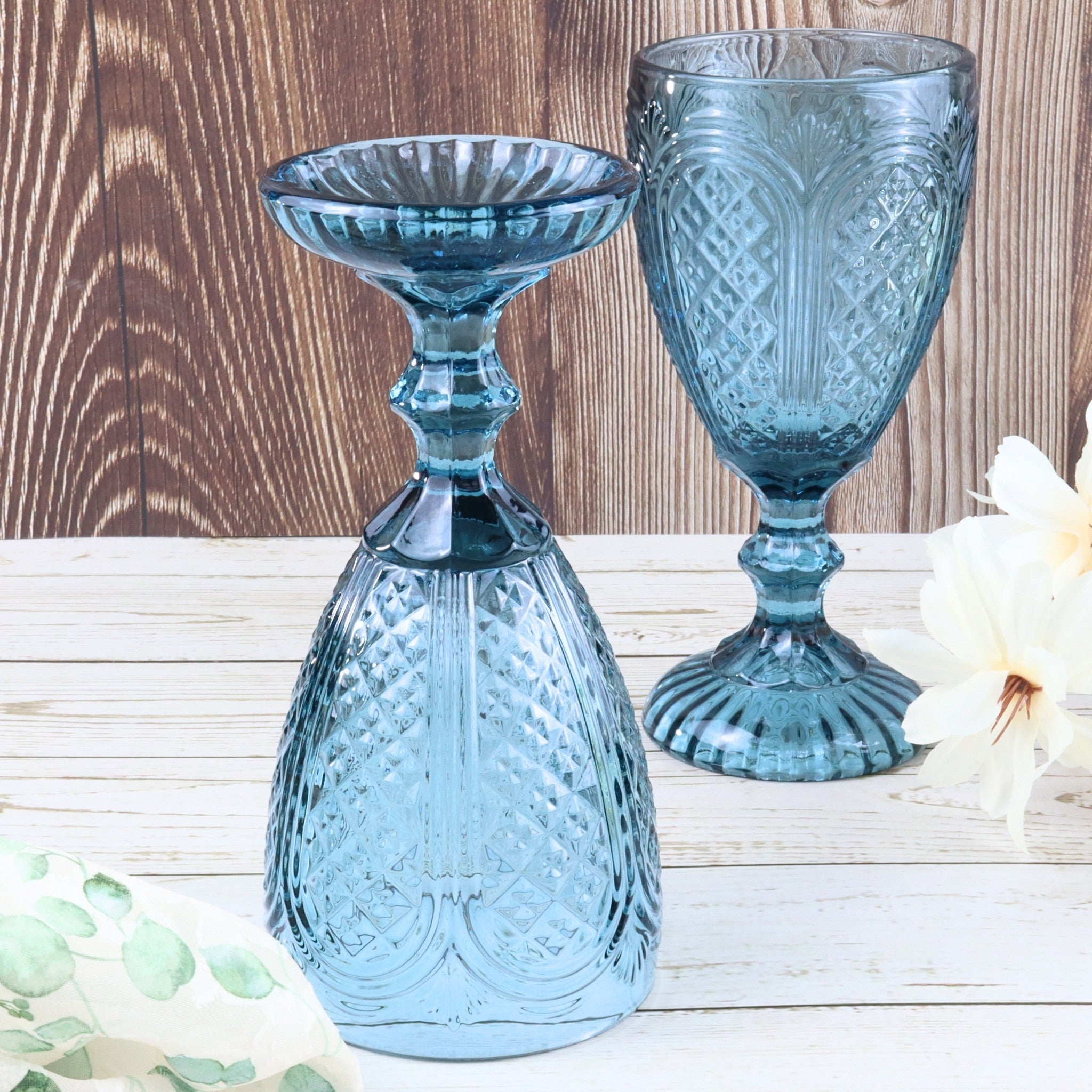 Set of six blue glass goblets on a white surface with a white curtain background