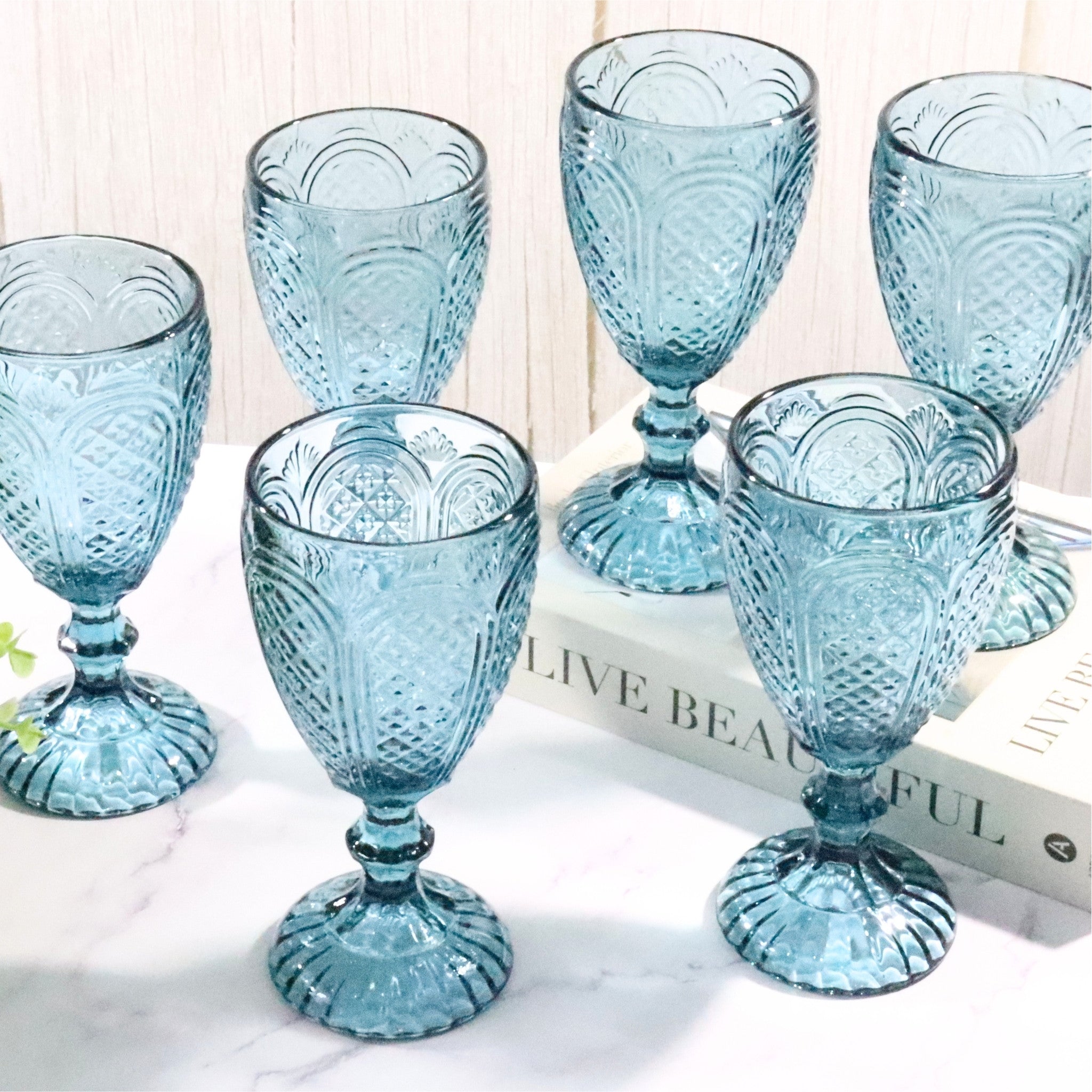 Set of blue glass goblets on a white surface with a book underneath.