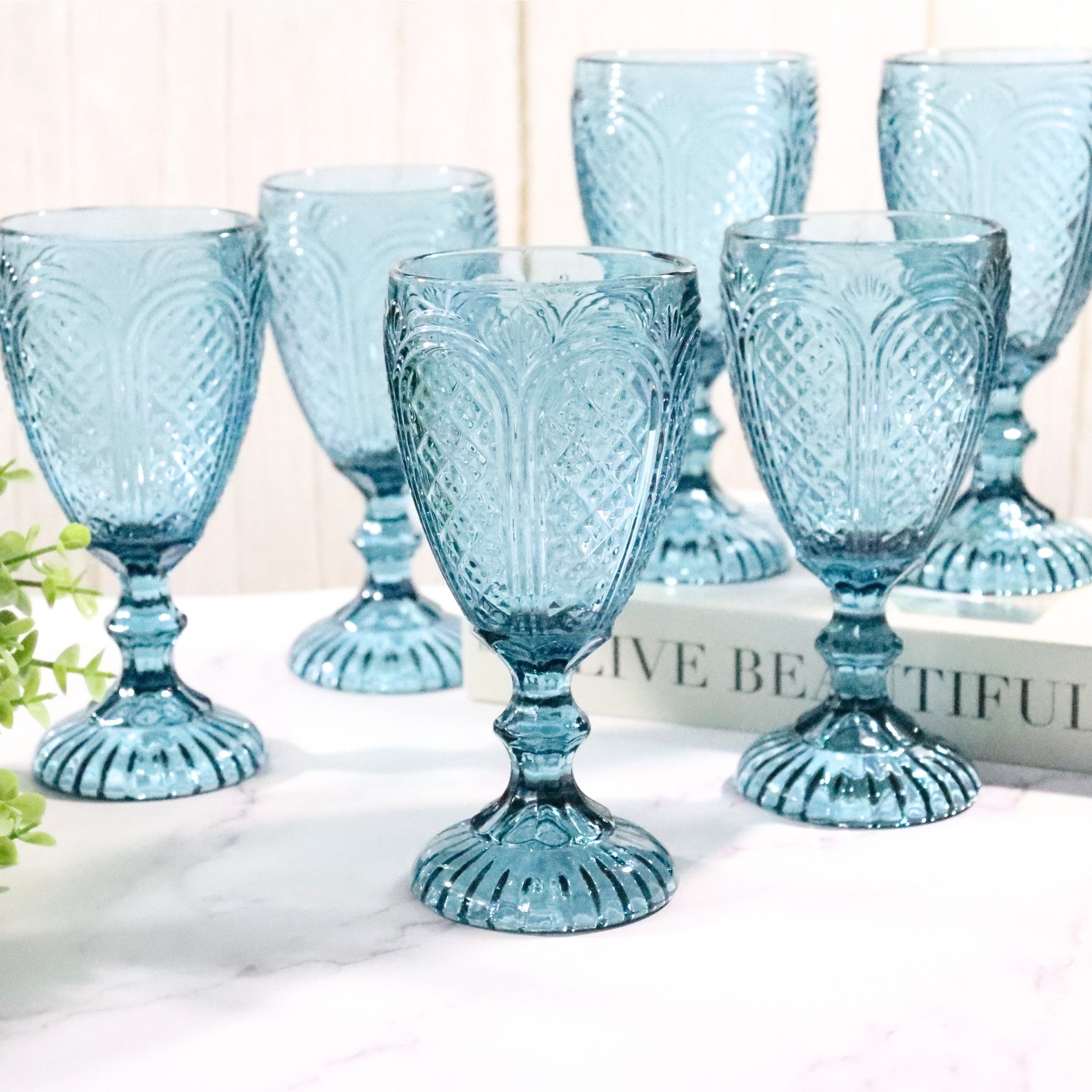Set of six blue glass goblets with embossed designs on a white surface.