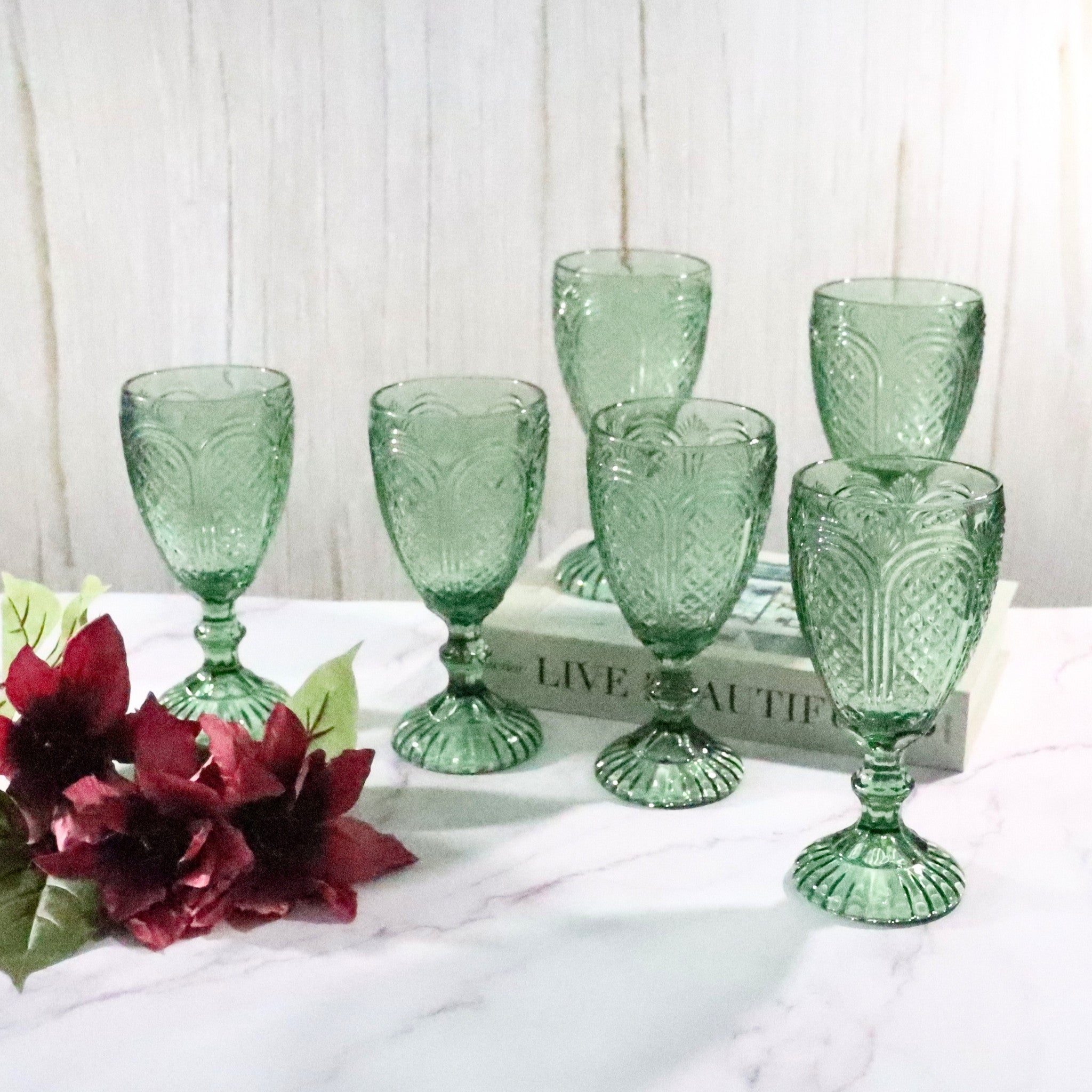 Set of green glass goblets on a white surface with flowers and a decorative box in the background.