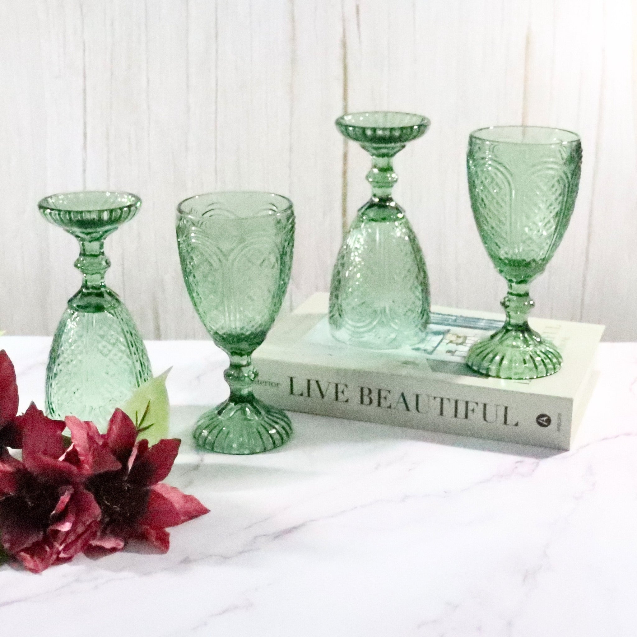Set of green glass goblets on a white surface with a book and flowers.