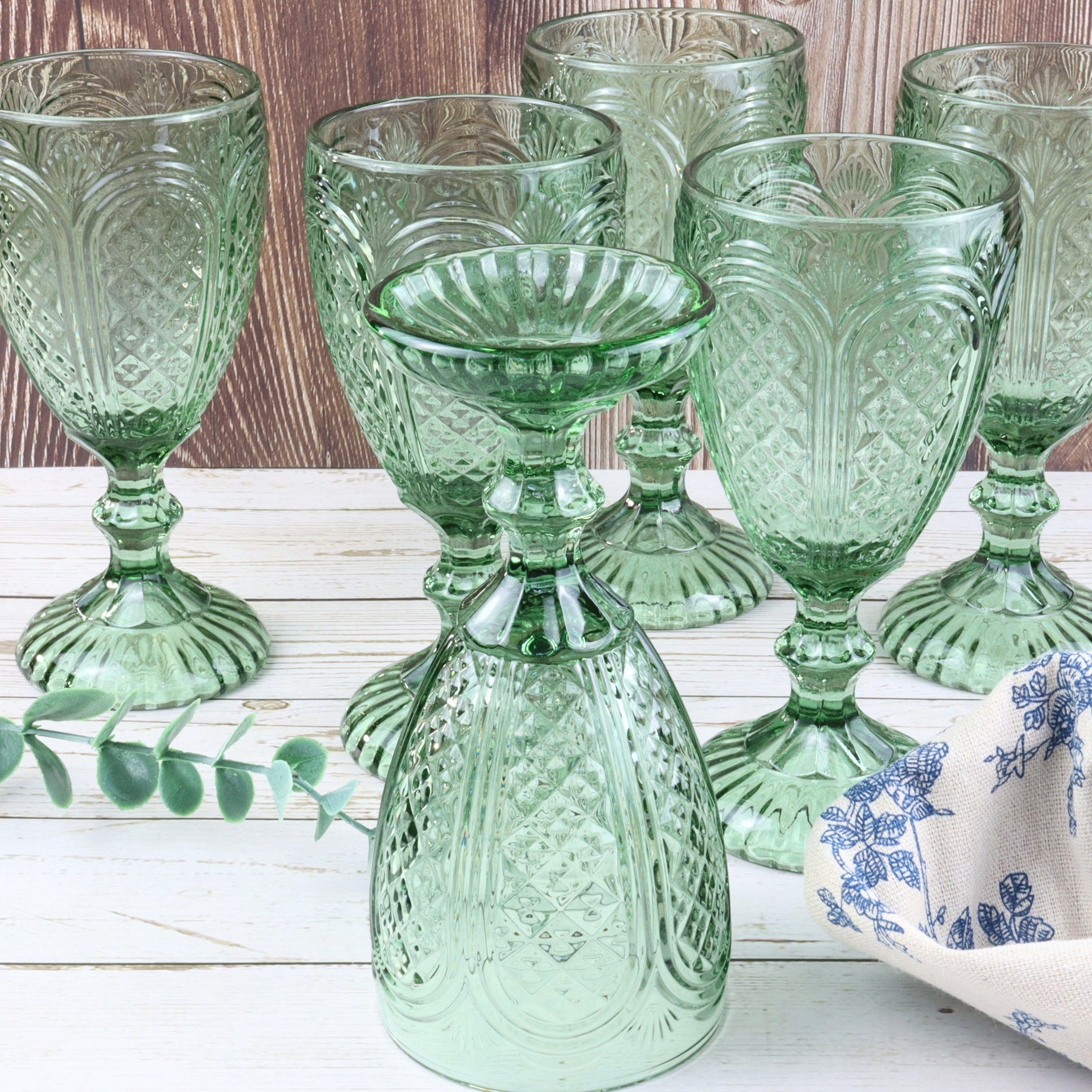 Set of green glass goblets on a white surface with flowers and a book in the background.