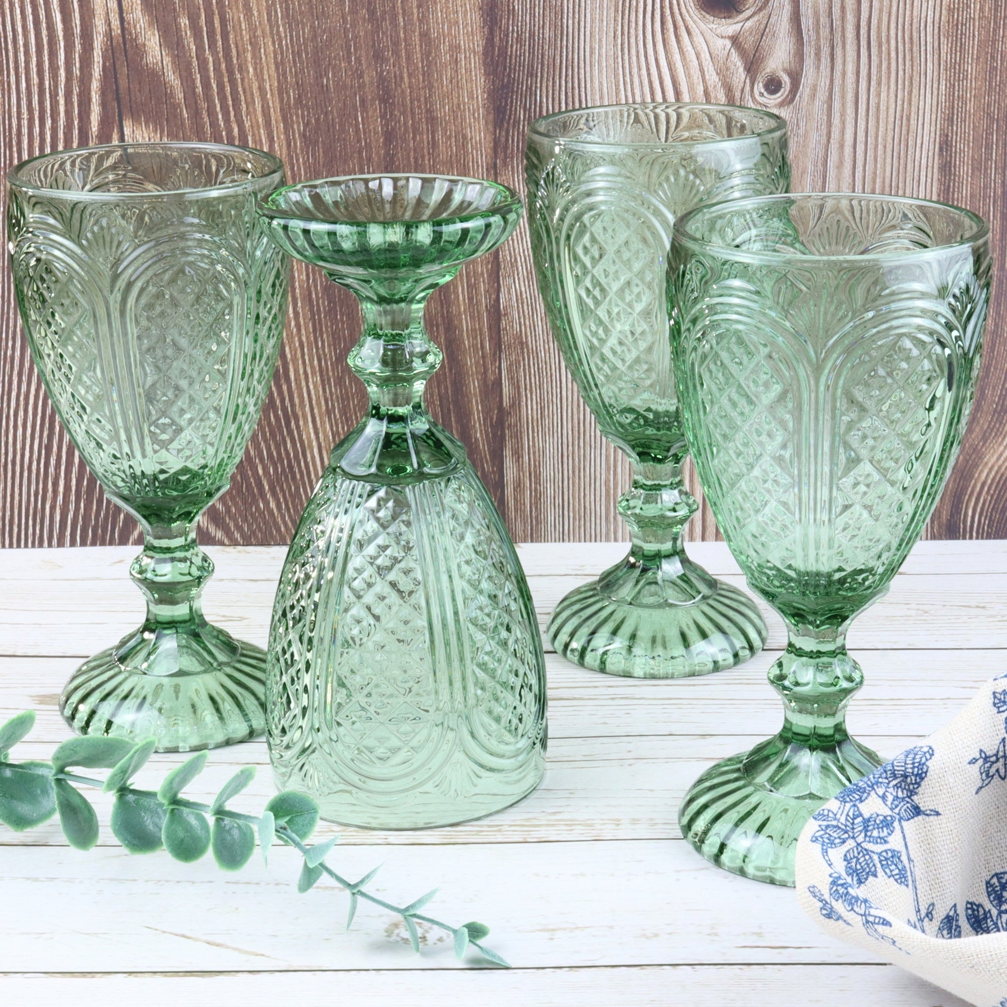 Set of green glass goblets on a white surface with flowers and a book in the background.