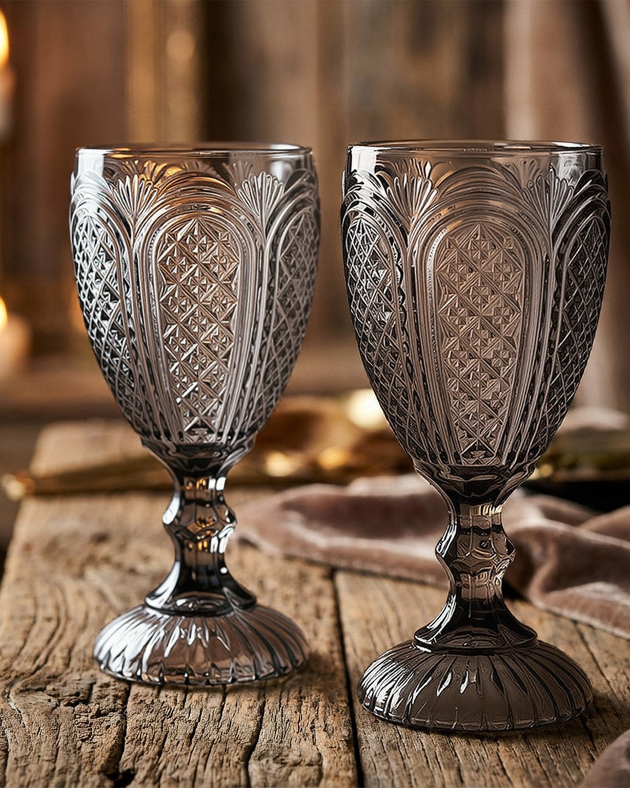 Two patterned glass goblets on a wooden surface with greenery in the background