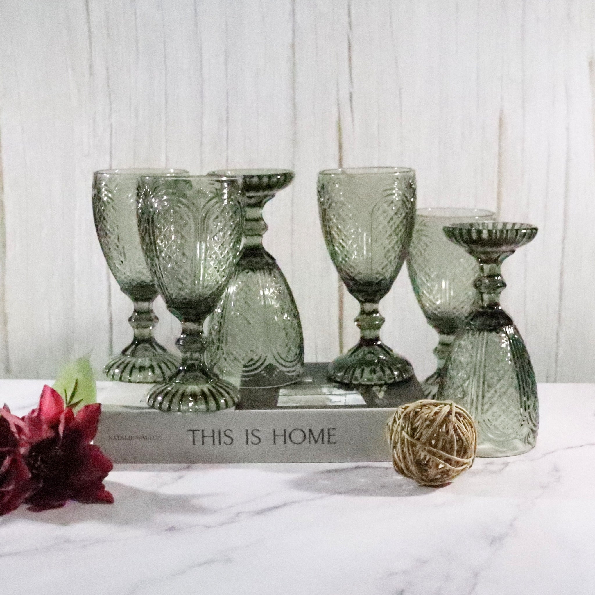 Set of grey glass goblets on a marble surface with a decorative book and flowers in the background.
