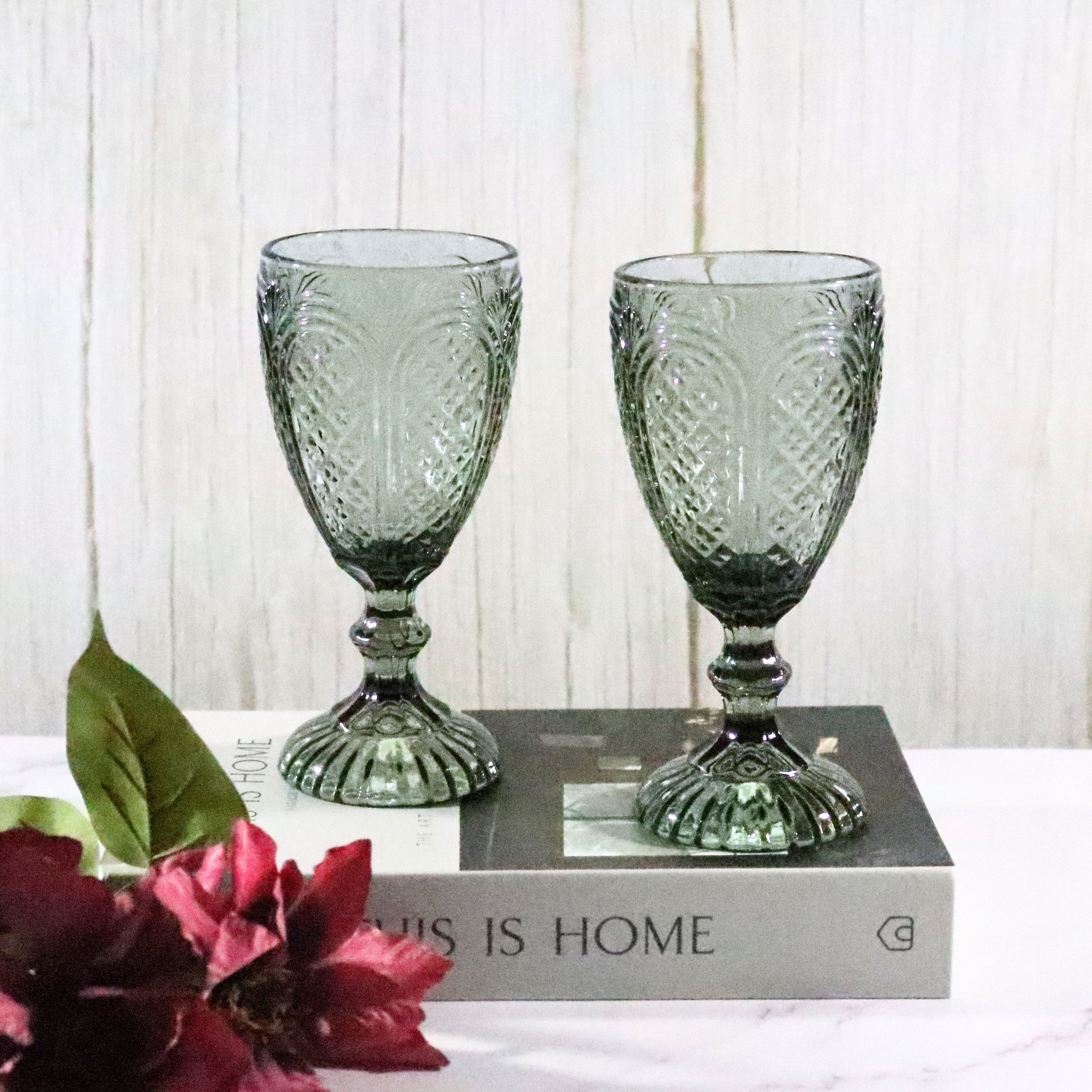 Two grey embossed textured glass goblets on a white surface with flowers and a book in the background.