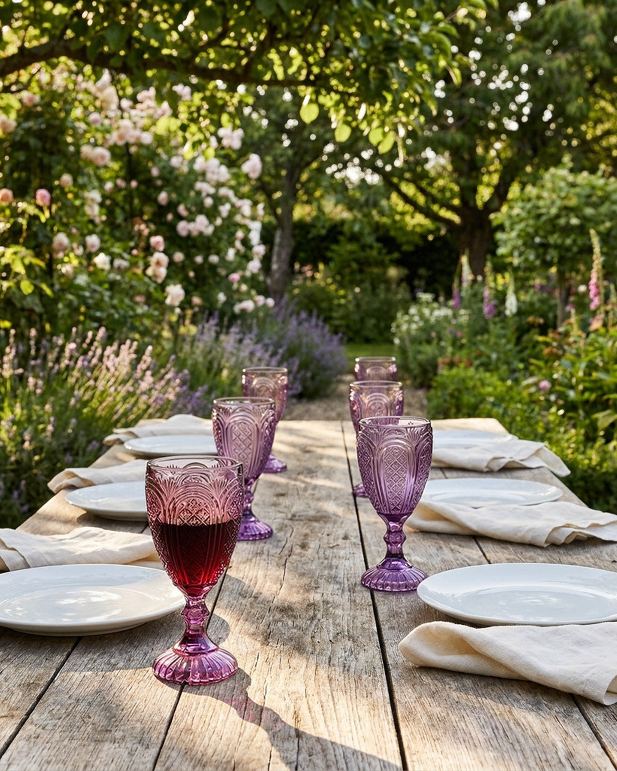 Two purple glass goblets on a white surface with red flowers and a book in the background.