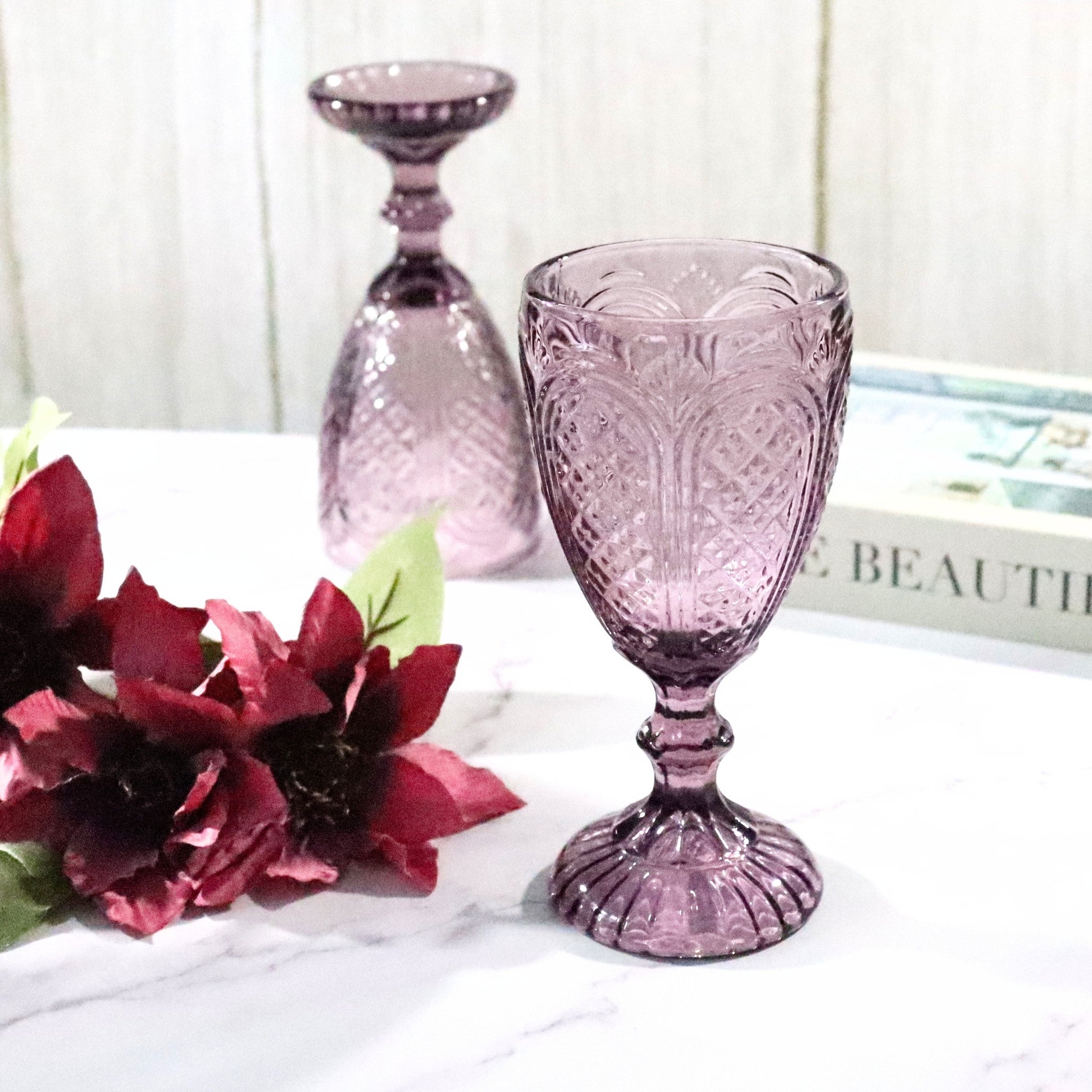 Pink glass goblet with floral arrangement on a white surface
